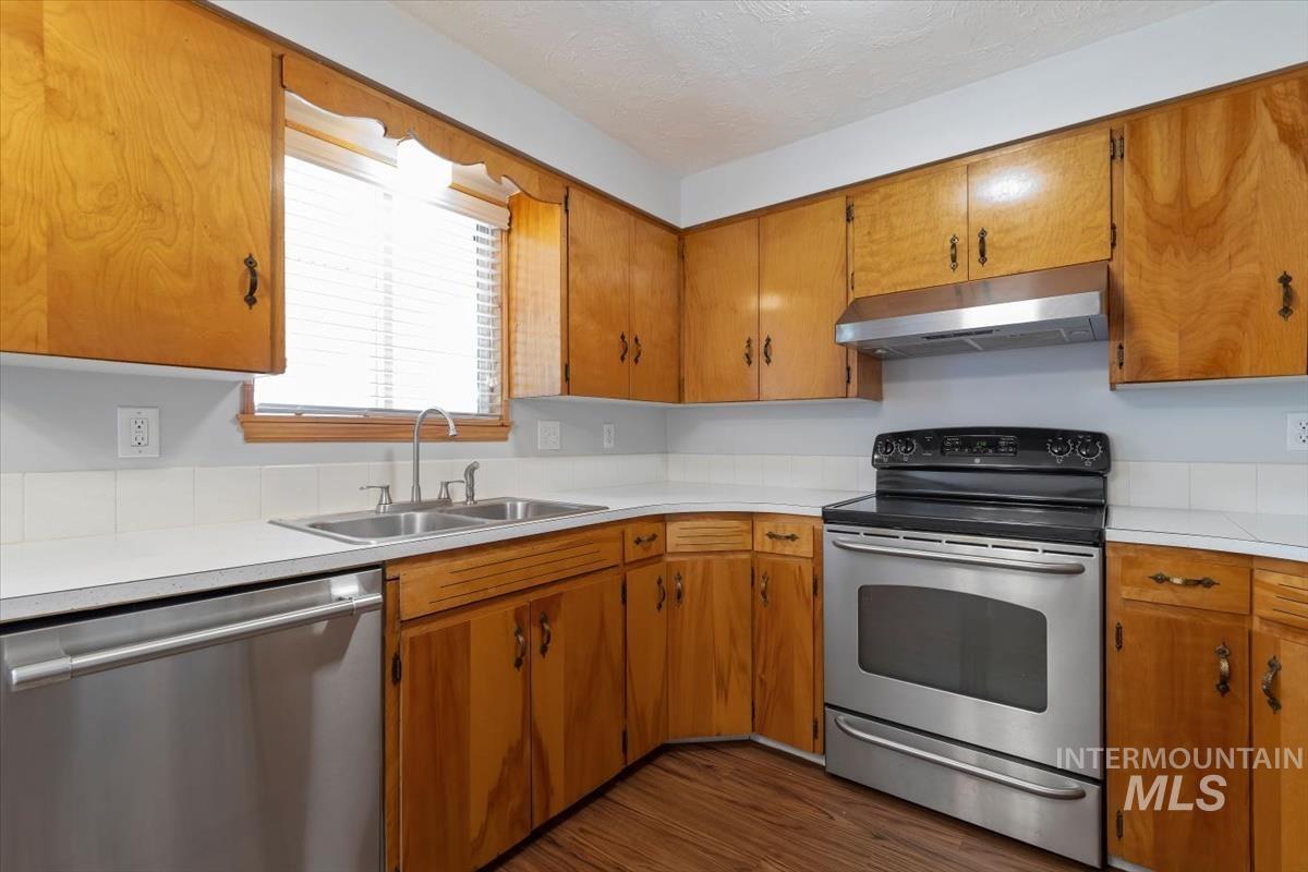 Kitchen featuring stainless steel appliances, under cabinet range hood, light countertops, and brown cabinets