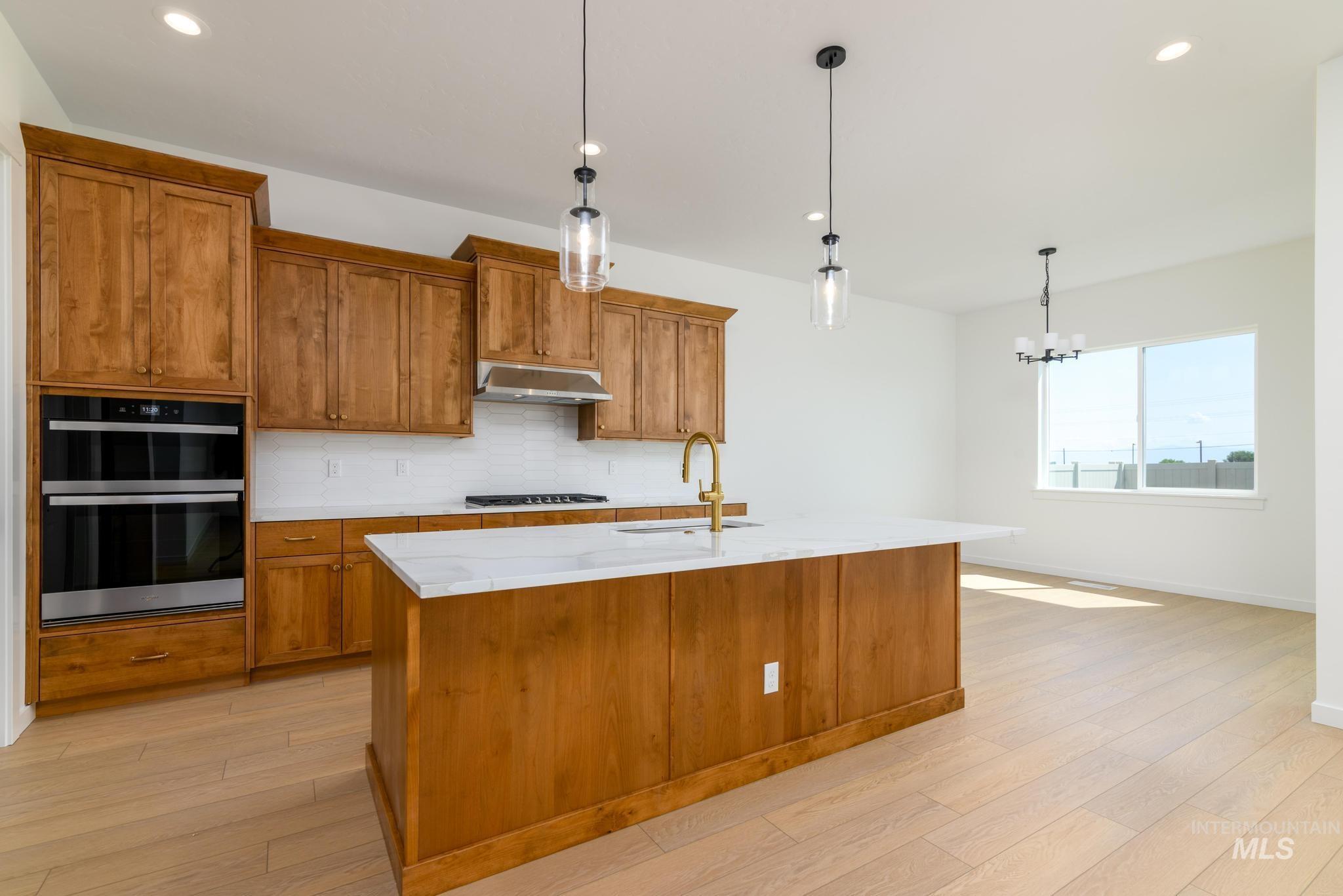 Kitchen with range hood, brown cabinets, light wood-type flooring, double oven, and backsplash