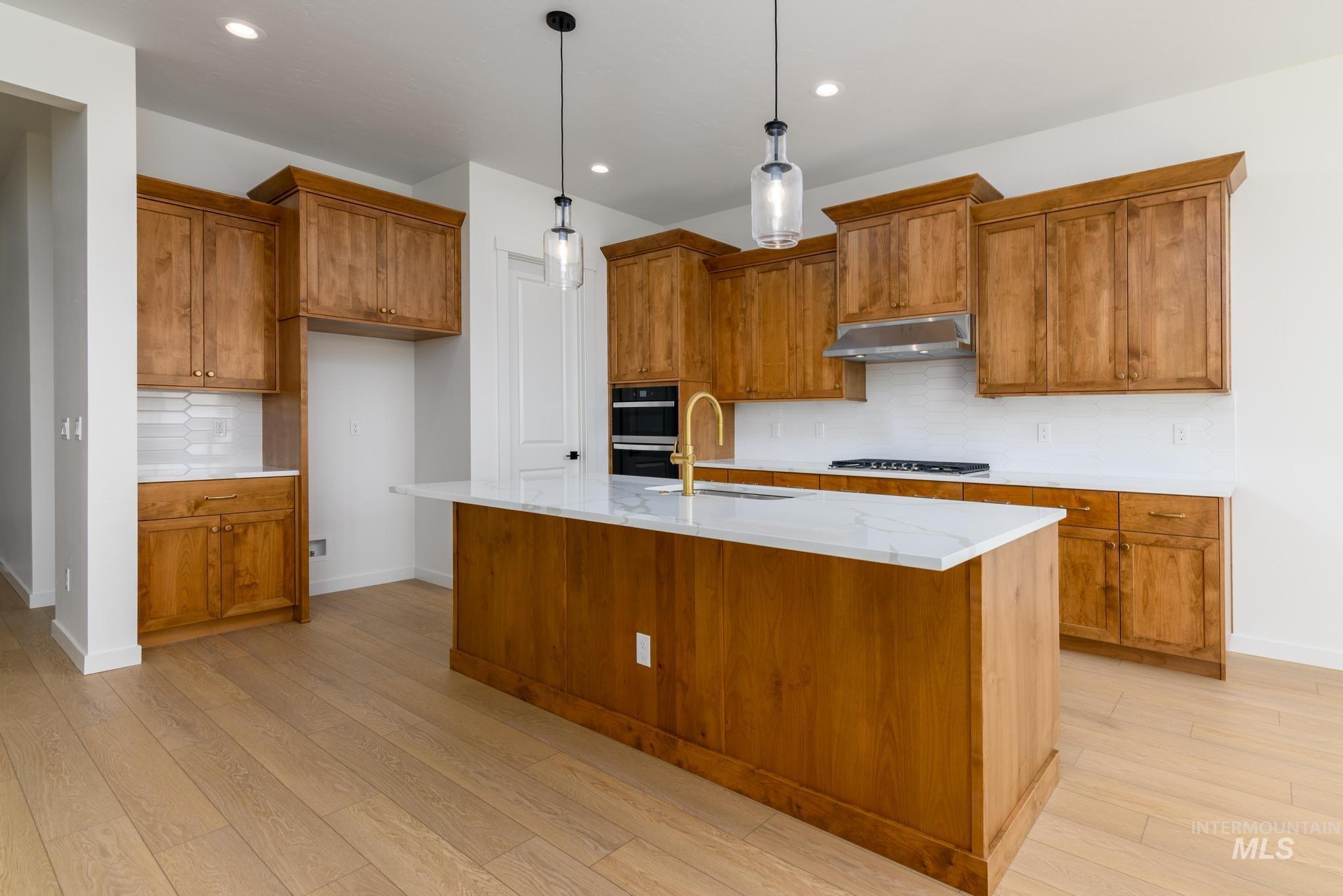 Kitchen with extractor fan, gas stovetop, brown cabinetry, light wood finished floors, and recessed lighting
