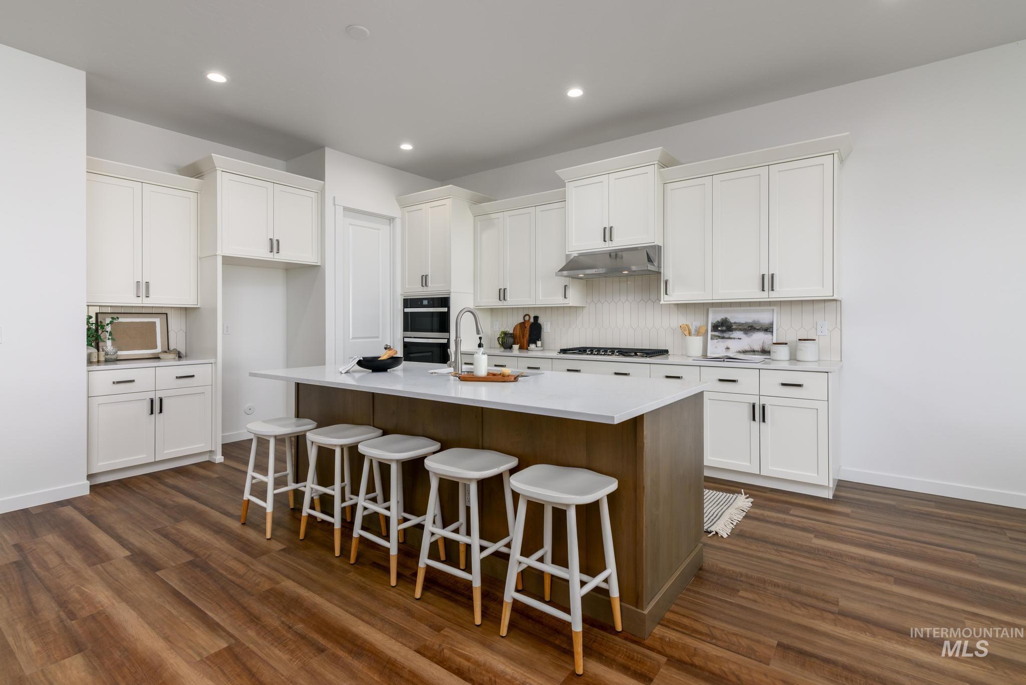 Kitchen with under cabinet range hood, stainless steel gas cooktop, dark wood-type flooring, white cabinetry, and recessed lighting