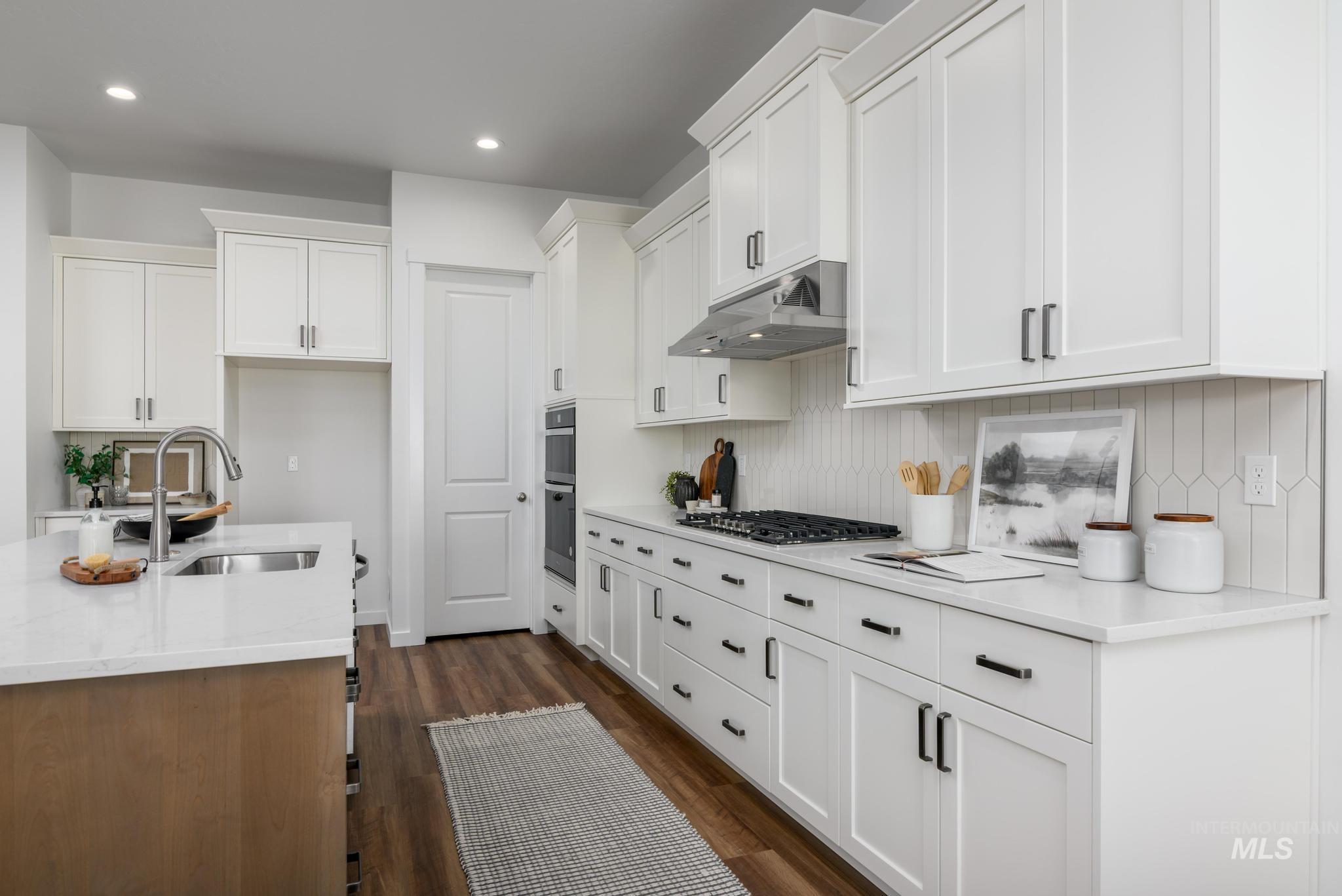 Kitchen featuring under cabinet range hood, decorative backsplash, white cabinets, dark wood-style flooring, and recessed lighting