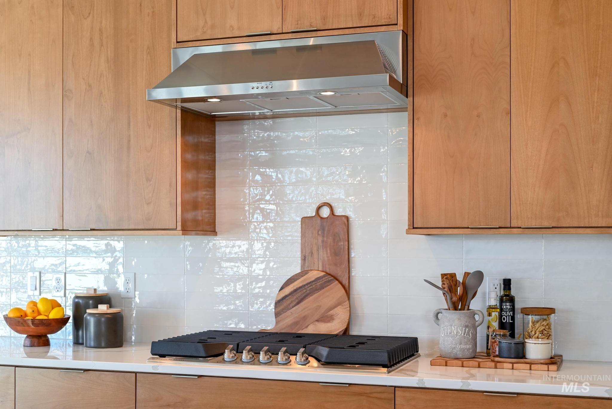 Kitchen featuring backsplash, exhaust hood, light stone countertops, stainless steel gas cooktop, and modern cabinets