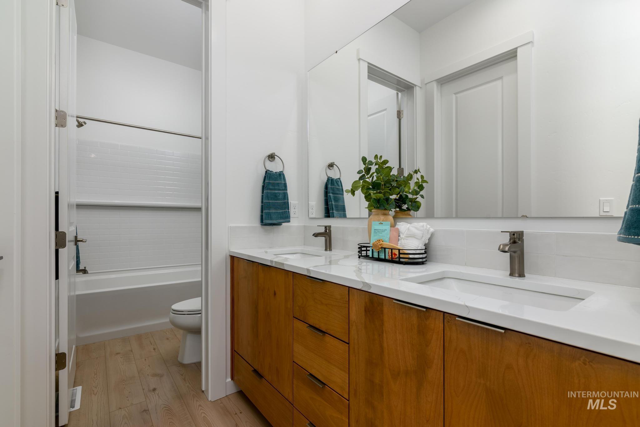 Full bath featuring light wood-style flooring, double vanity, and shower / tub combination