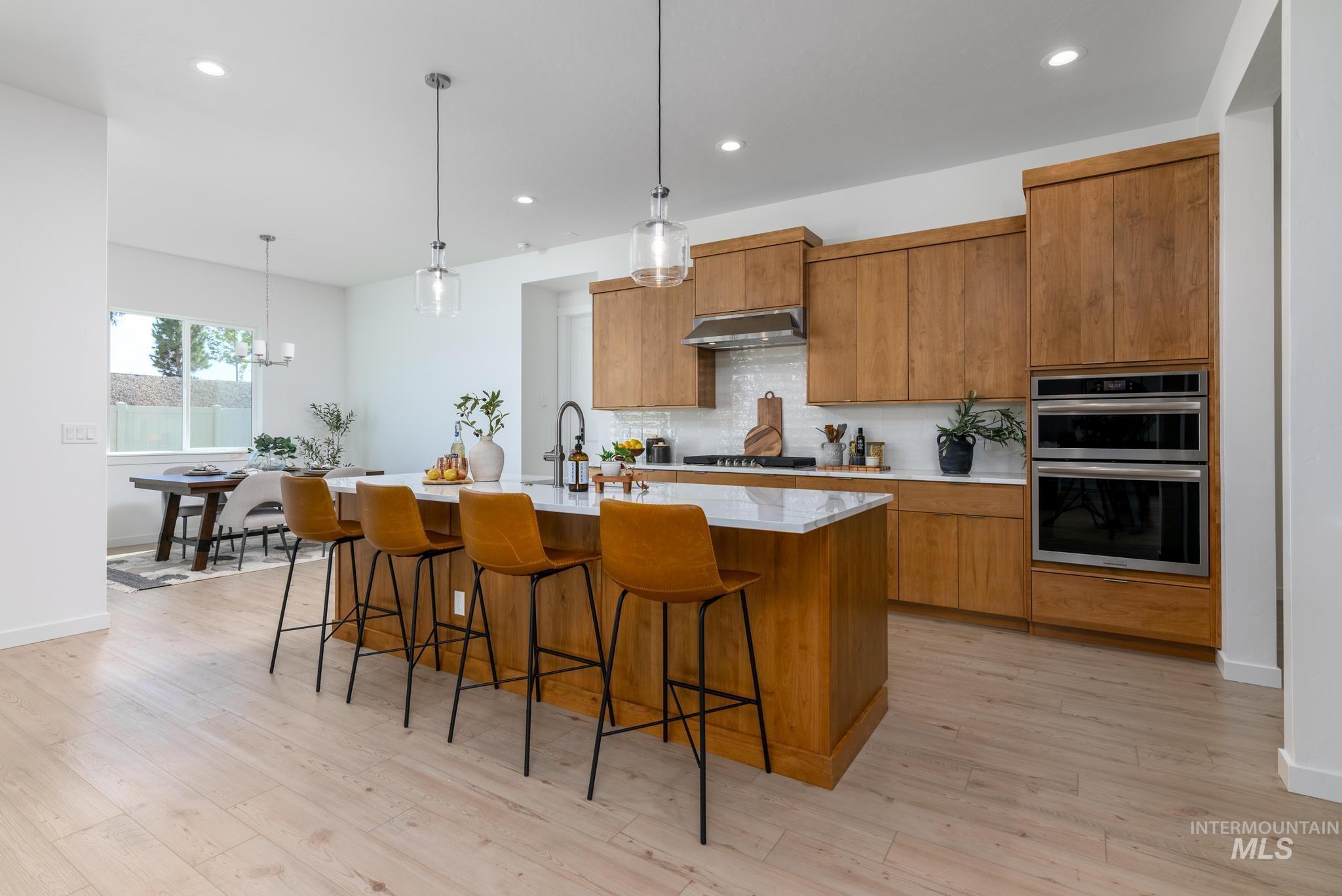 Kitchen with brown cabinetry, backsplash, hanging light fixtures, light stone counters, and recessed lighting