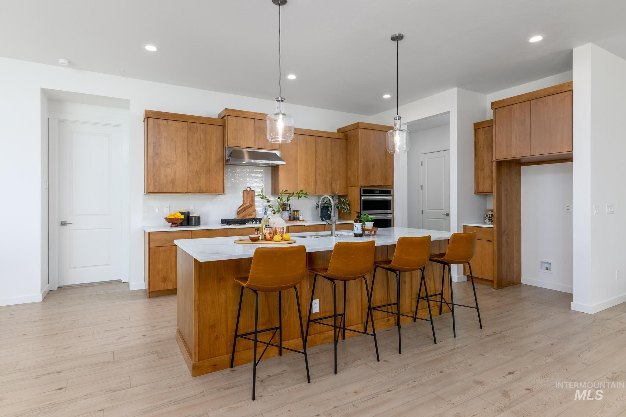 Kitchen featuring brown cabinets, hanging light fixtures, a breakfast bar, a center island with sink, and light stone countertops