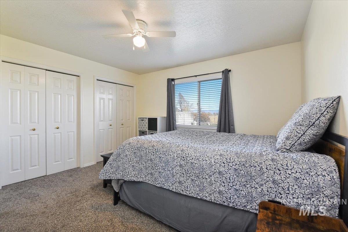 Bedroom with multiple closets, a textured ceiling, dark colored carpet, and ceiling fan