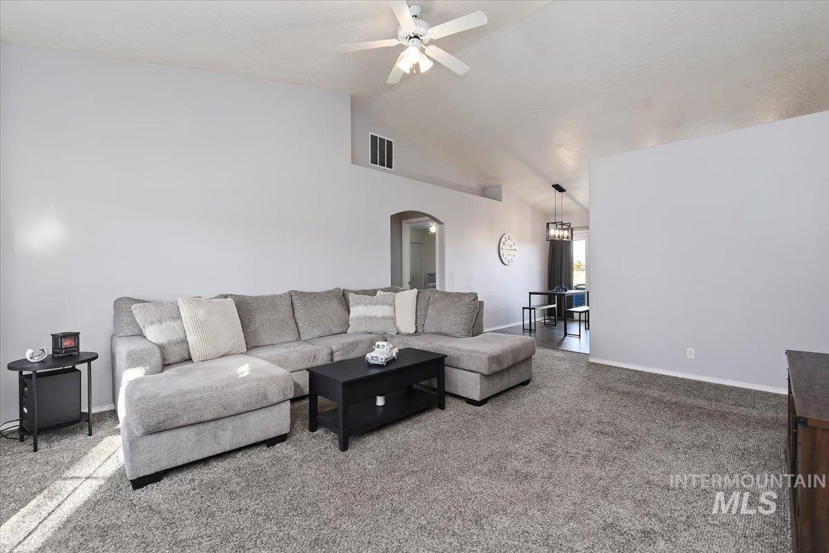 Carpeted living area featuring lofted ceiling, arched walkways, and ceiling fan