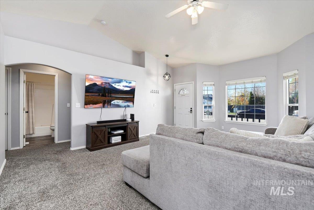 Living room featuring carpet, lofted ceiling, arched walkways, and ceiling fan