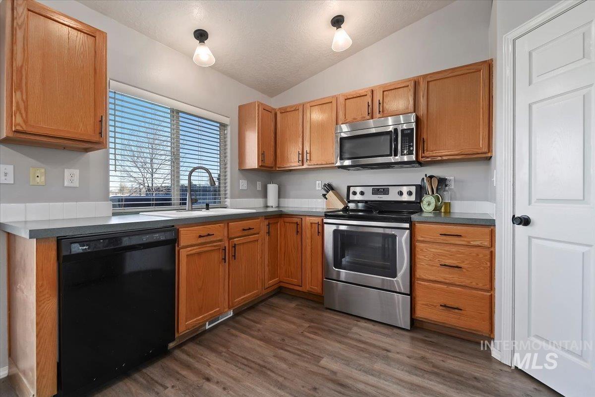 Kitchen with appliances with stainless steel finishes, vaulted ceiling, dark wood finished floors, a textured ceiling, and brown cabinets
