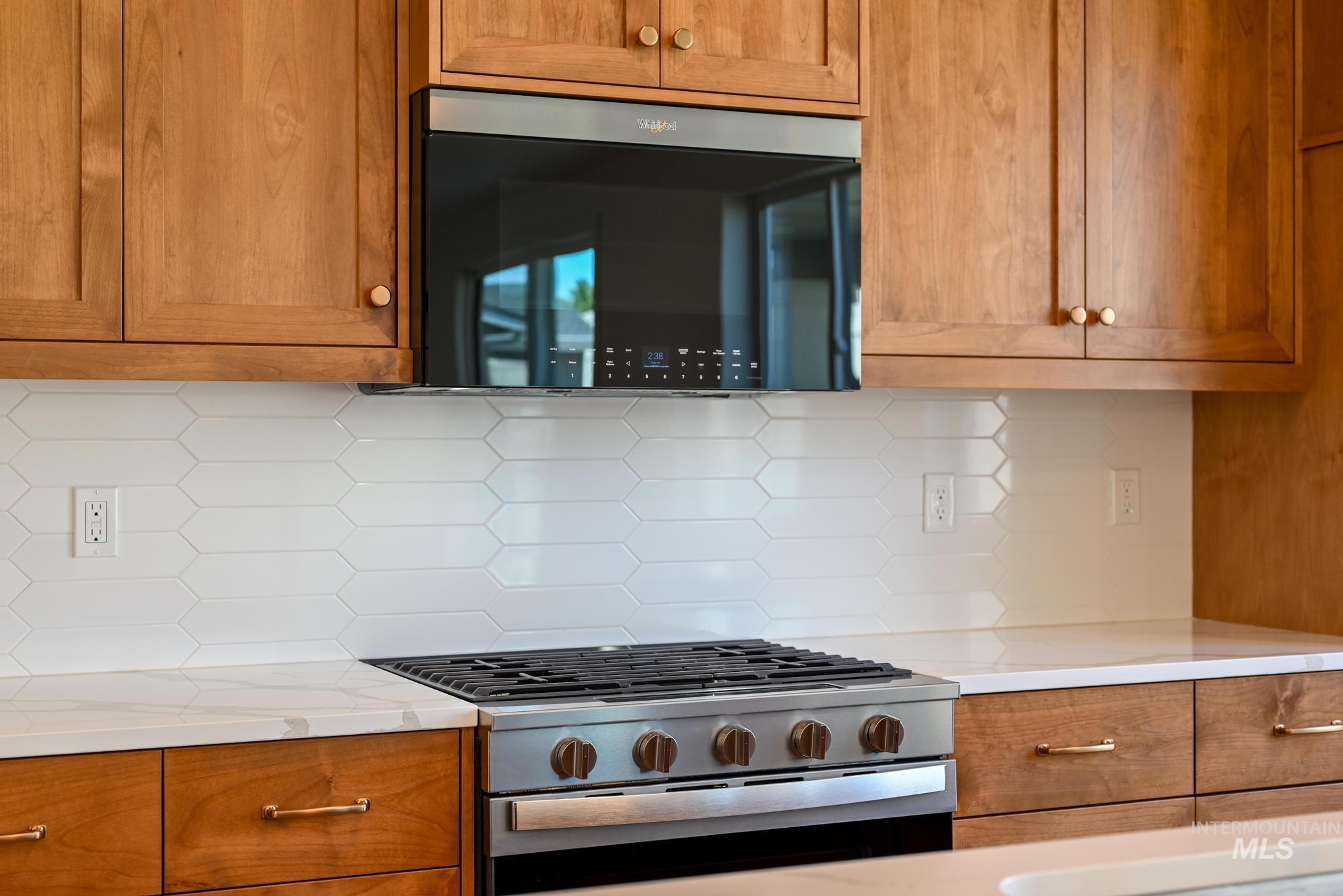 Kitchen featuring stainless steel gas range oven, backsplash, and brown cabinetry