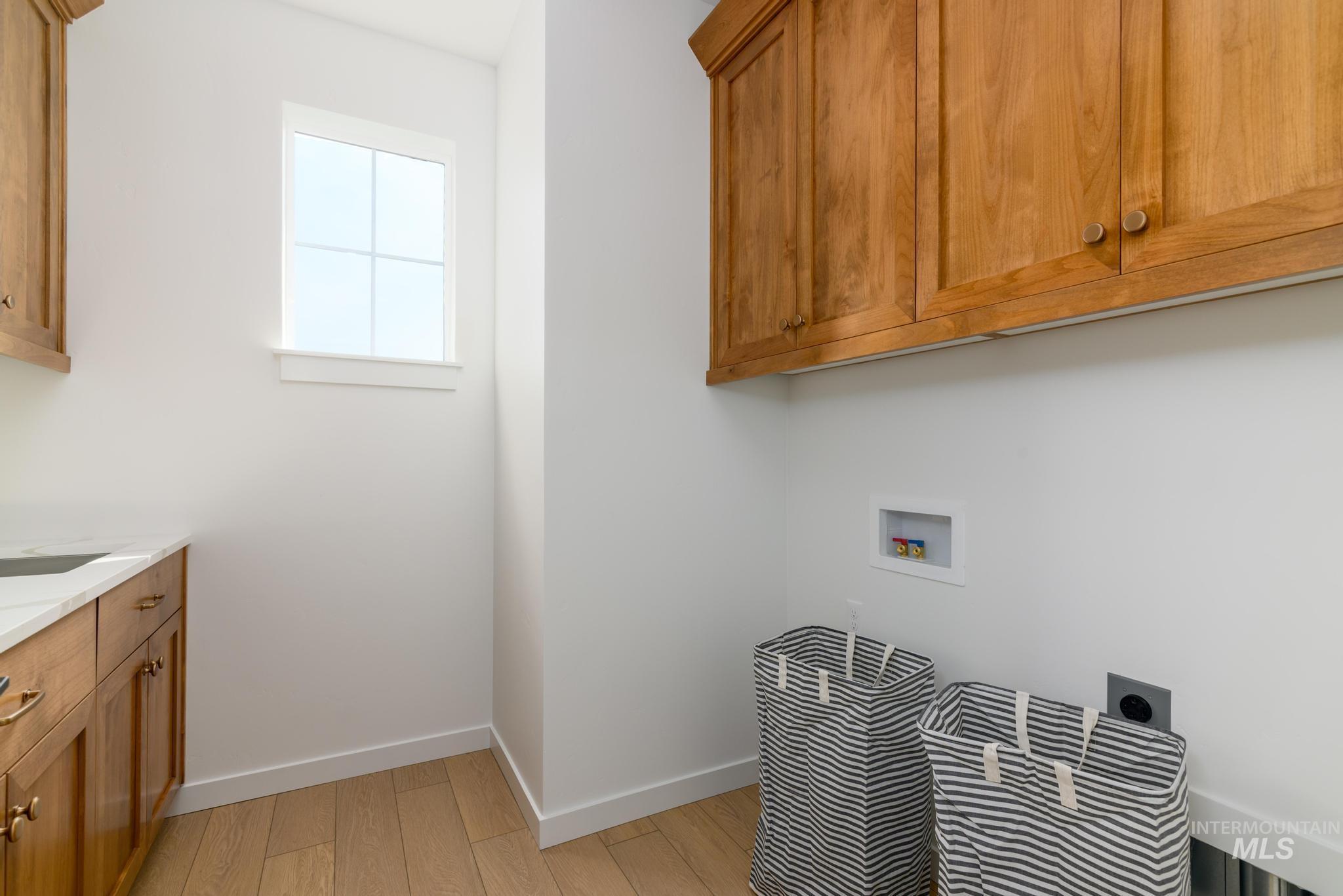 Laundry area featuring light wood-style flooring, washer hookup, and cabinet space