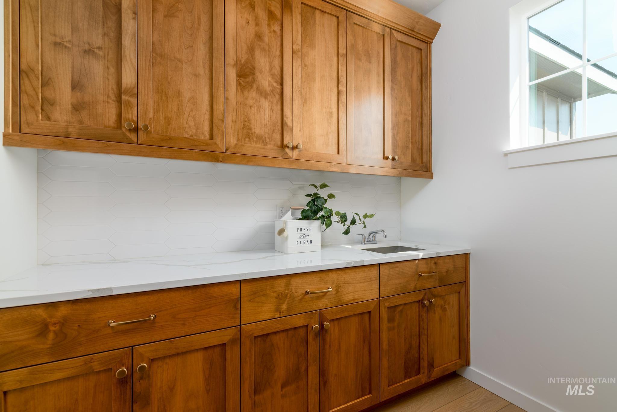 Bar featuring brown cabinetry, tasteful backsplash, light stone counters, and light wood-style flooring