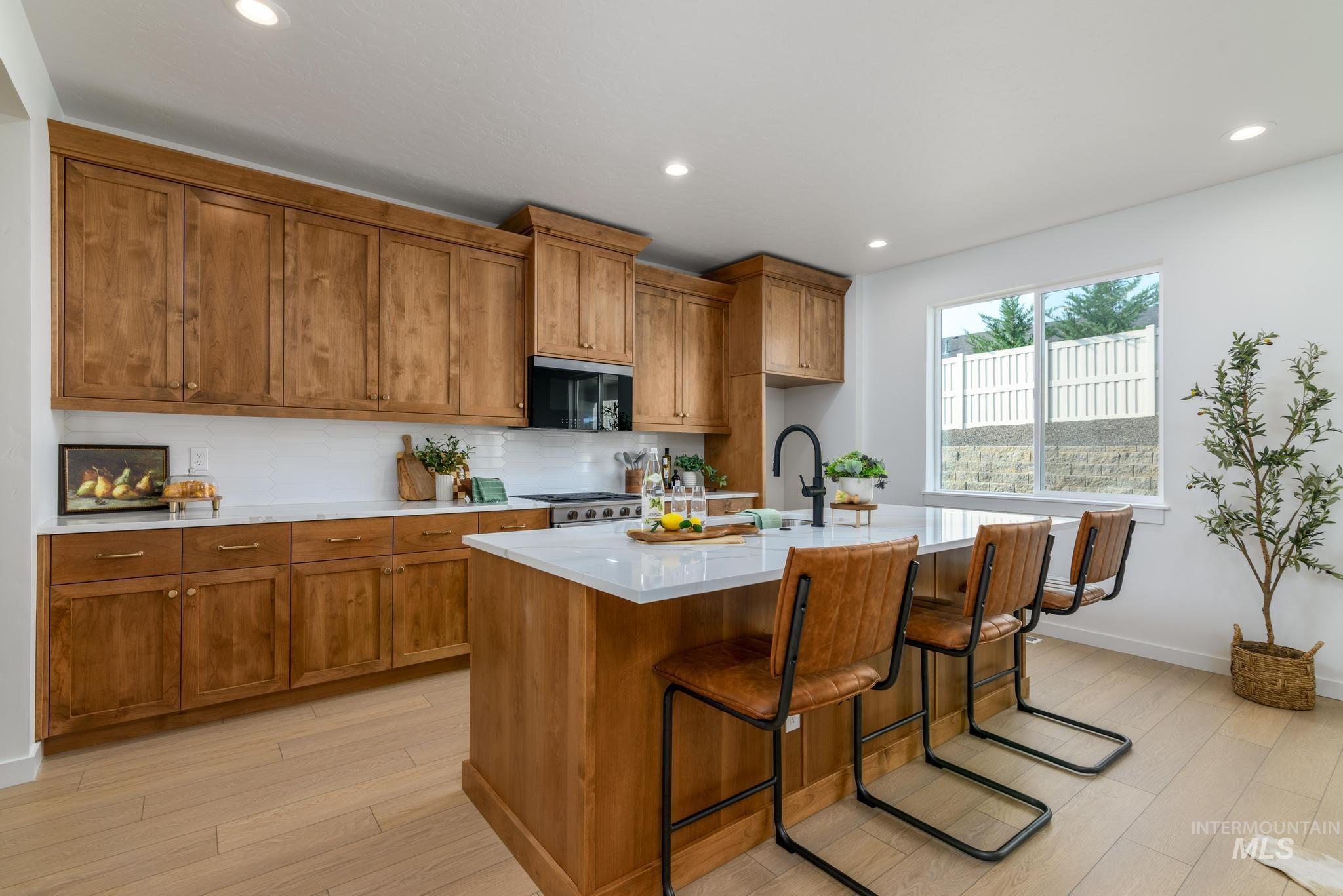 Kitchen with brown cabinets, a breakfast bar, recessed lighting, a kitchen island with sink, and light wood finished floors