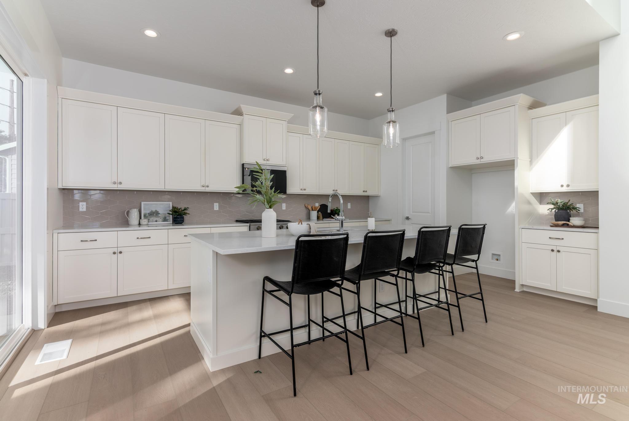 Kitchen with decorative backsplash, a kitchen breakfast bar, hanging light fixtures, a center island with sink, and white cabinets
