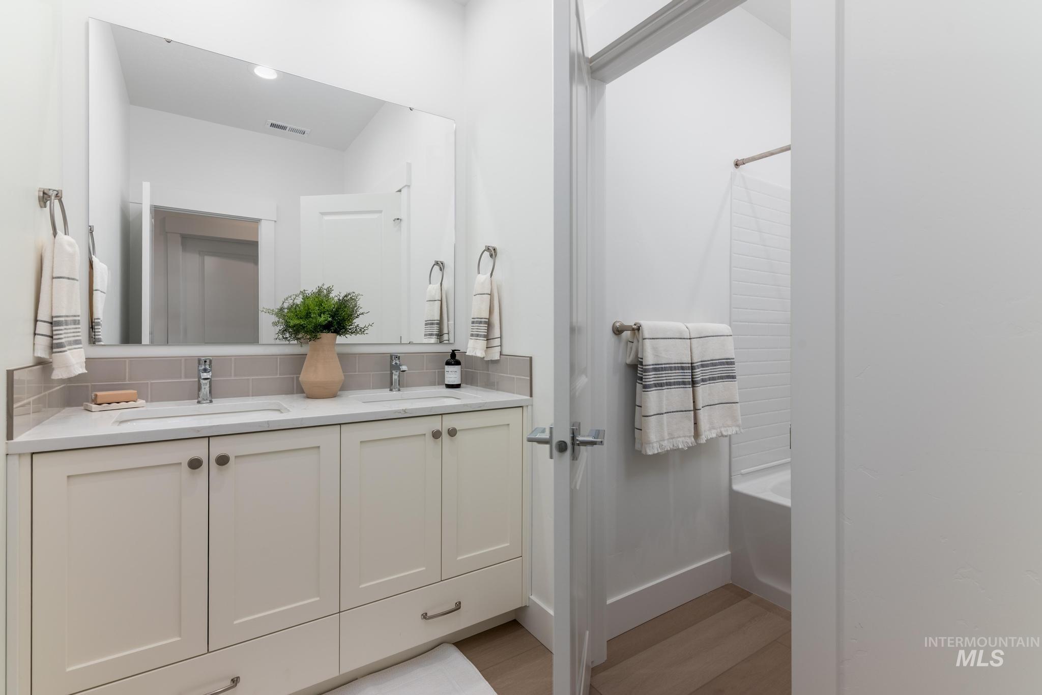 Bathroom with double vanity, light wood-style floors, and shower / tub combo