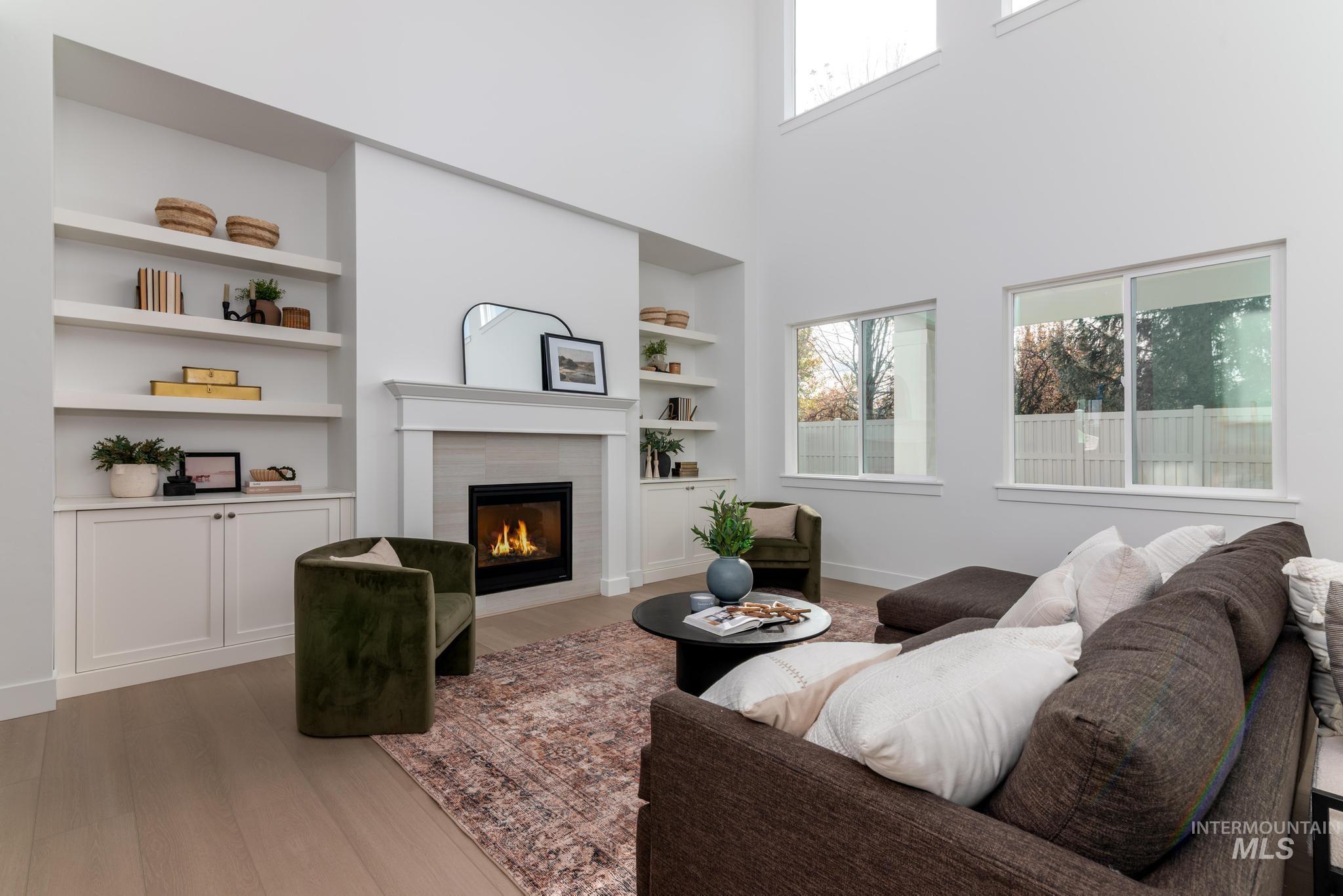 Living room with built in features, light wood finished floors, a tile fireplace, and a high ceiling