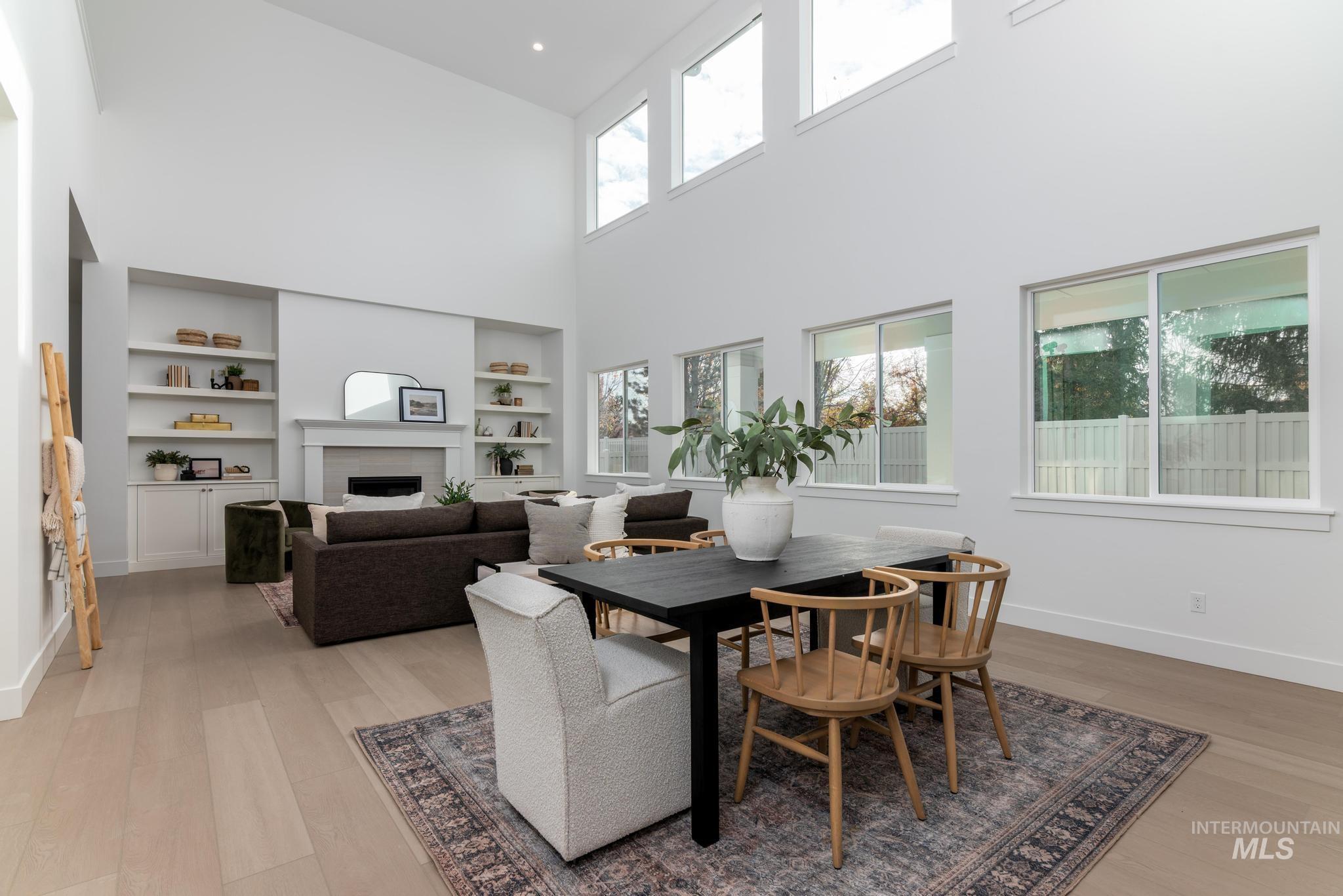 Dining space featuring a fireplace, light wood-style floors, healthy amount of natural light, built in features, and a towering ceiling