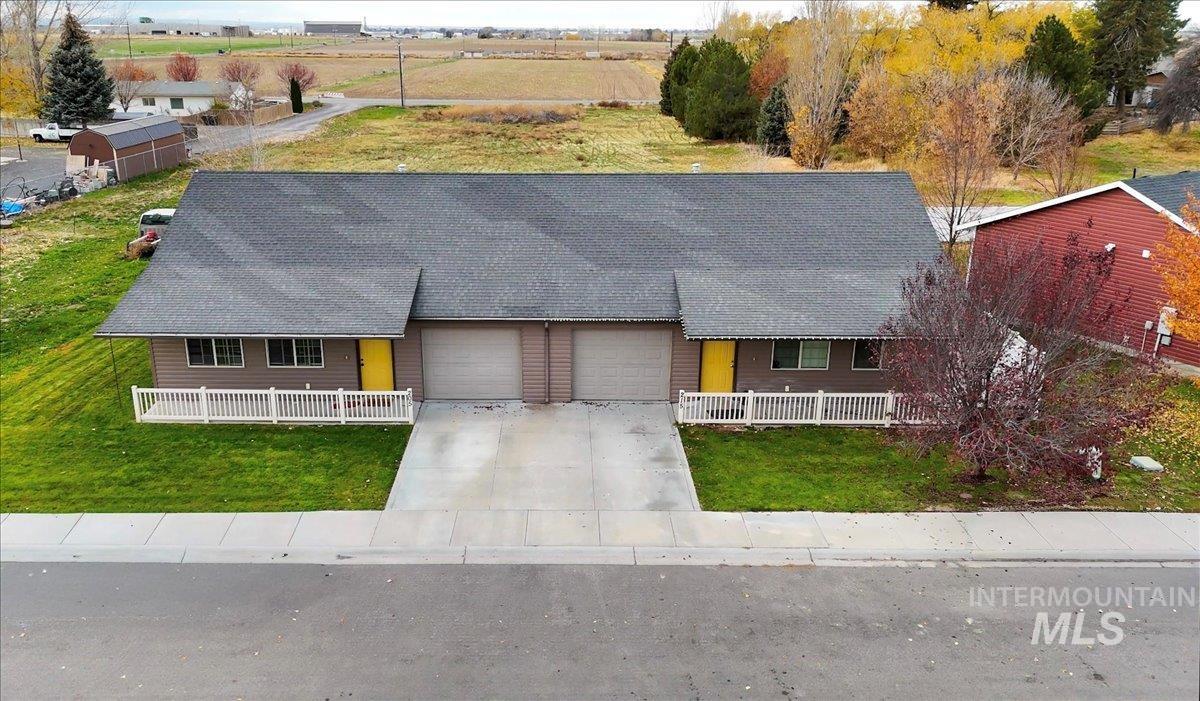 View of front facade featuring a front lawn, driveway, a shingled roof, a view of rural / pastoral area, and an attached garage