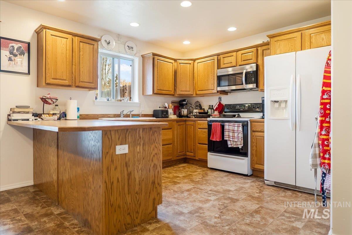 Kitchen with white appliances, a peninsula, brown cabinetry, light countertops, and recessed lighting