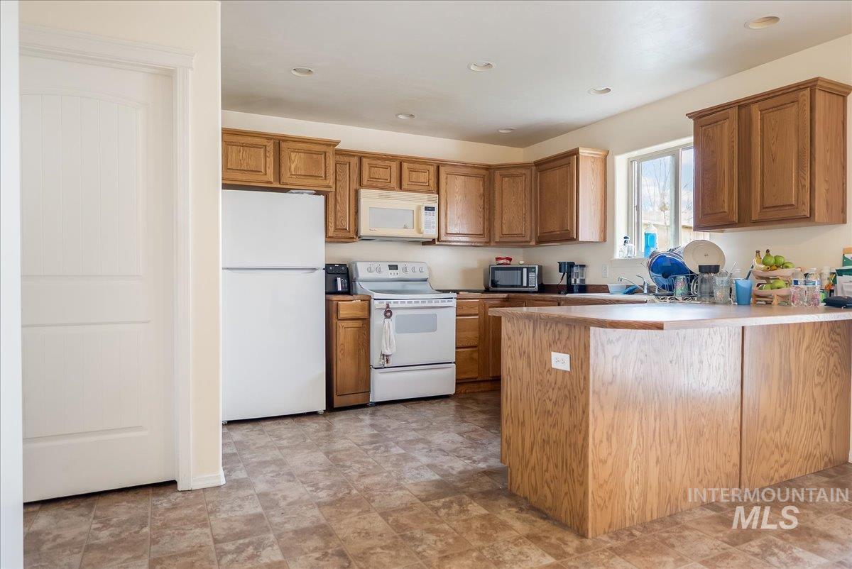 Kitchen featuring white appliances, brown cabinets, a peninsula, light countertops, and recessed lighting