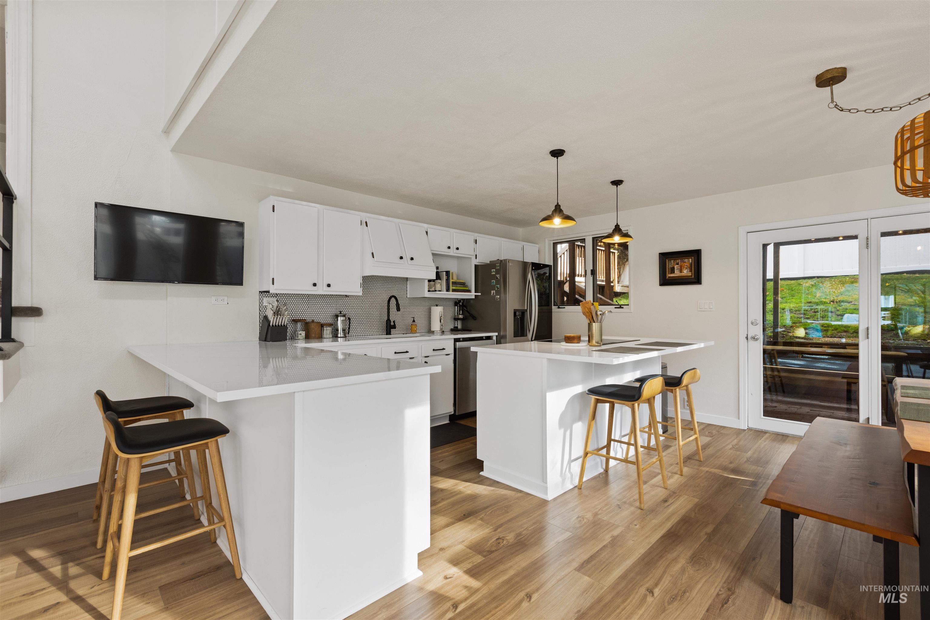 Kitchen featuring a kitchen breakfast bar, tasteful backsplash, decorative light fixtures, and white cabinetry