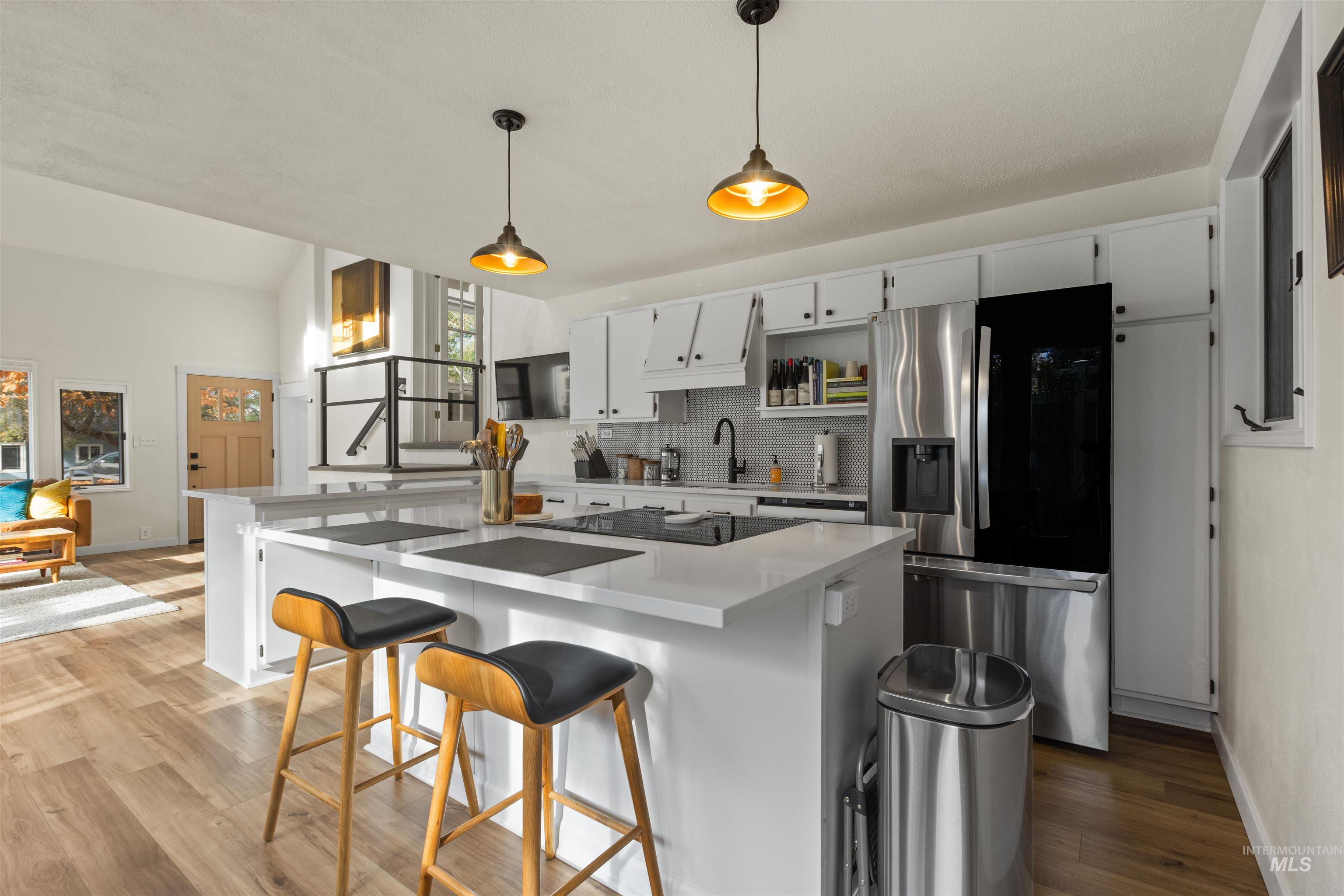 Kitchen with stainless steel refrigerator with ice dispenser, white cabinets, backsplash, a breakfast bar, and hanging light fixtures