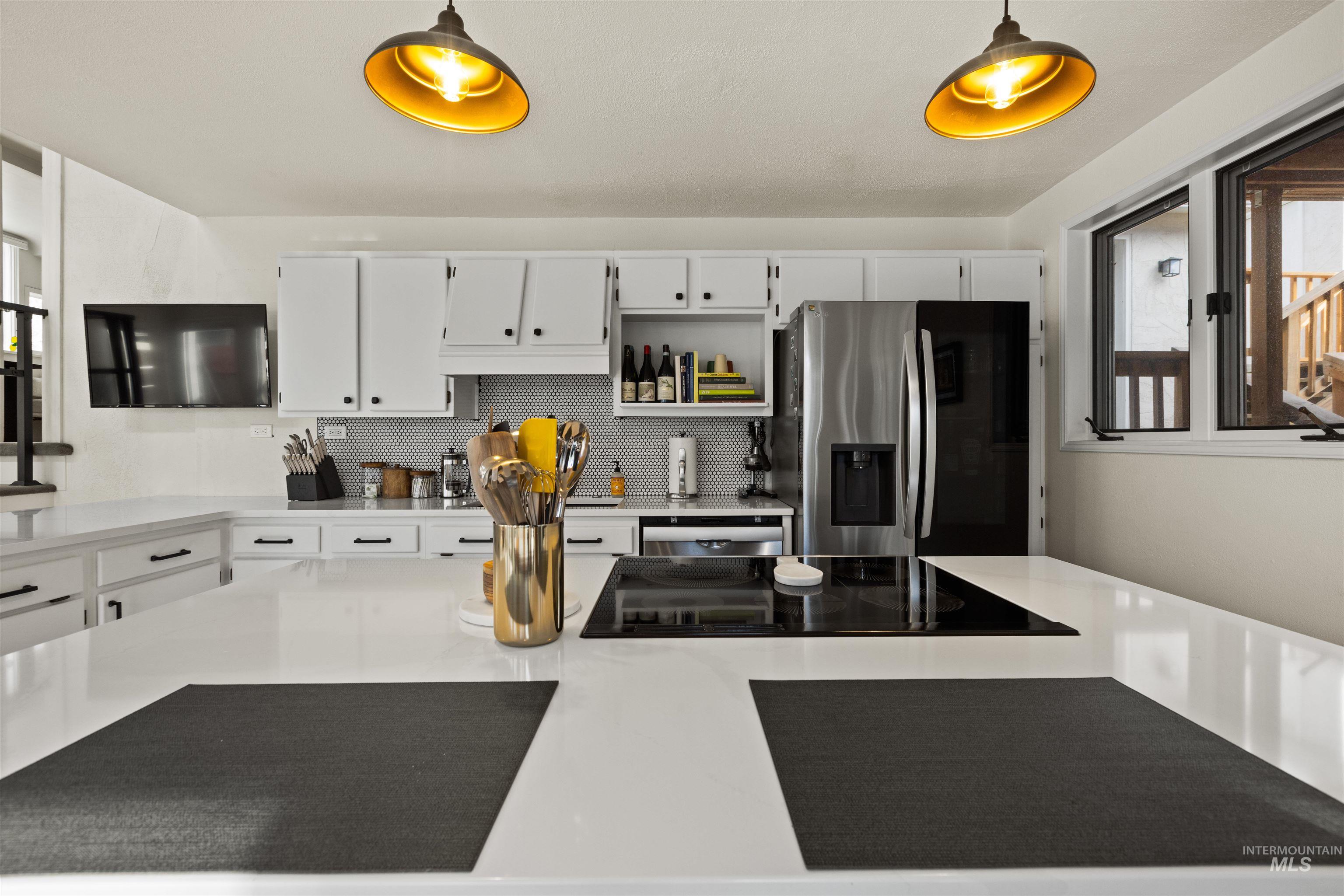Kitchen featuring decorative backsplash, stainless steel refrigerator with ice dispenser, white cabinets, black electric cooktop, and open shelves