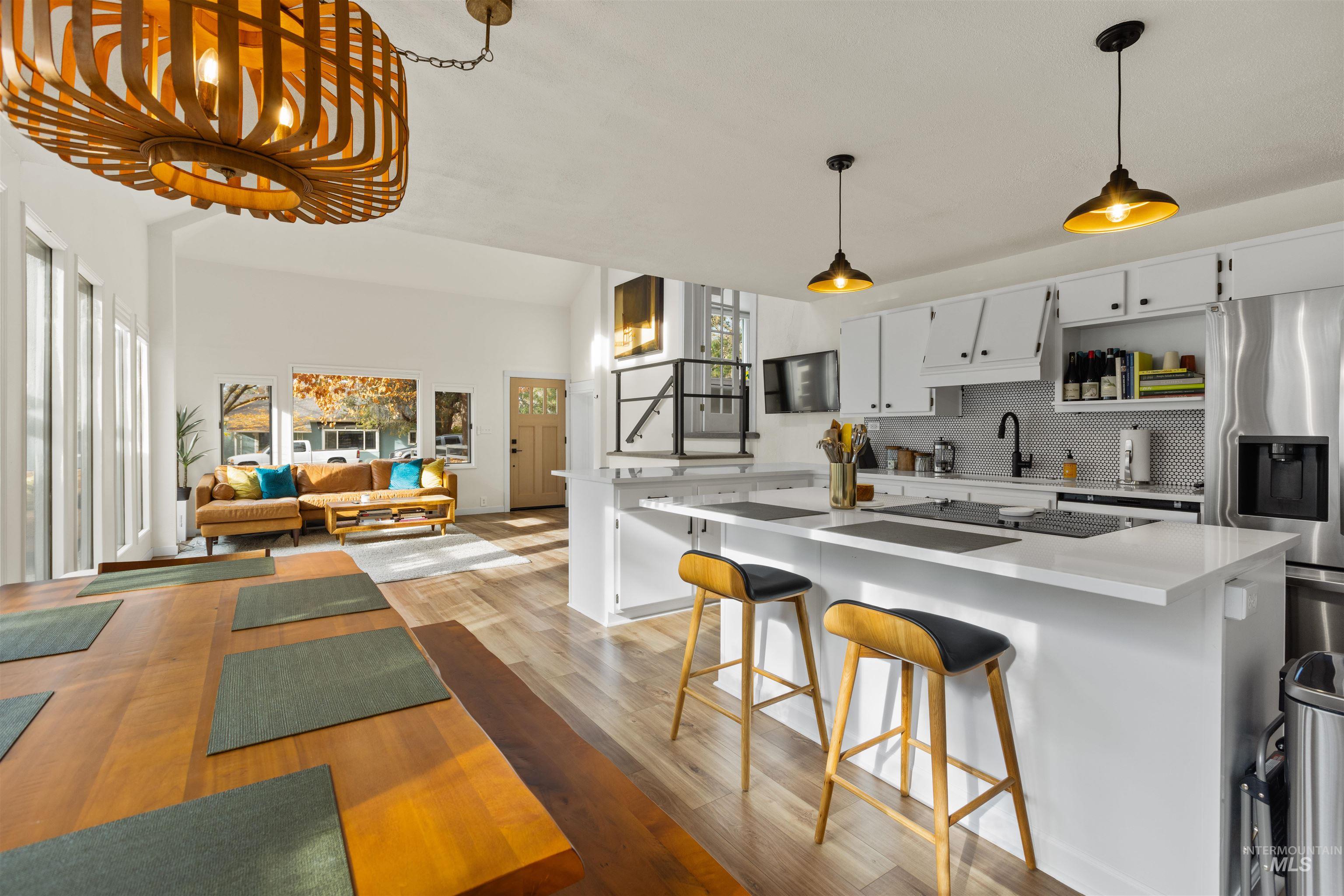 Kitchen featuring white cabinets, decorative backsplash, light wood-type flooring, decorative light fixtures, and stainless steel refrigerator with ice dispenser