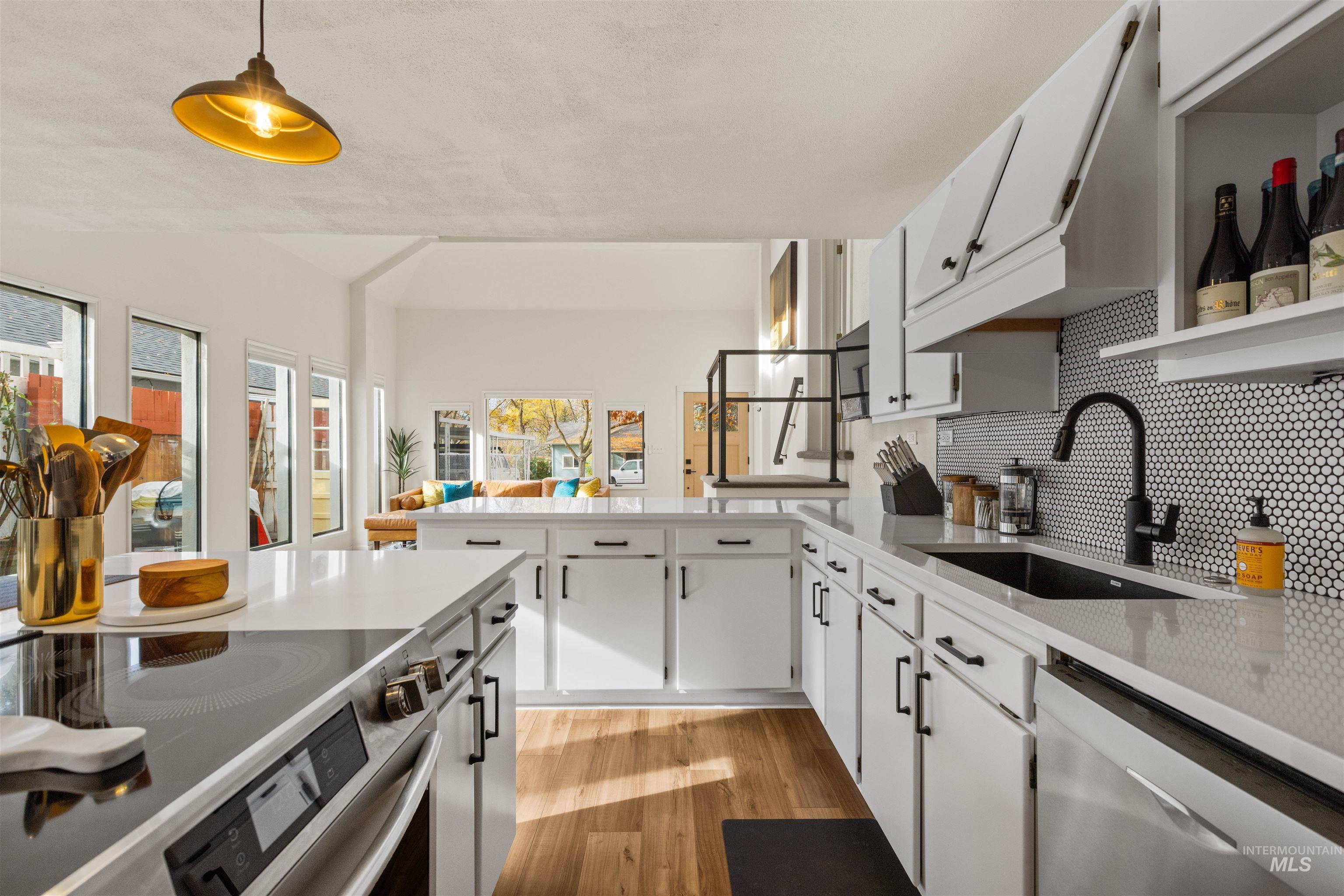 Kitchen featuring white cabinetry, light wood finished floors, appliances with stainless steel finishes, pendant lighting, and decorative backsplash