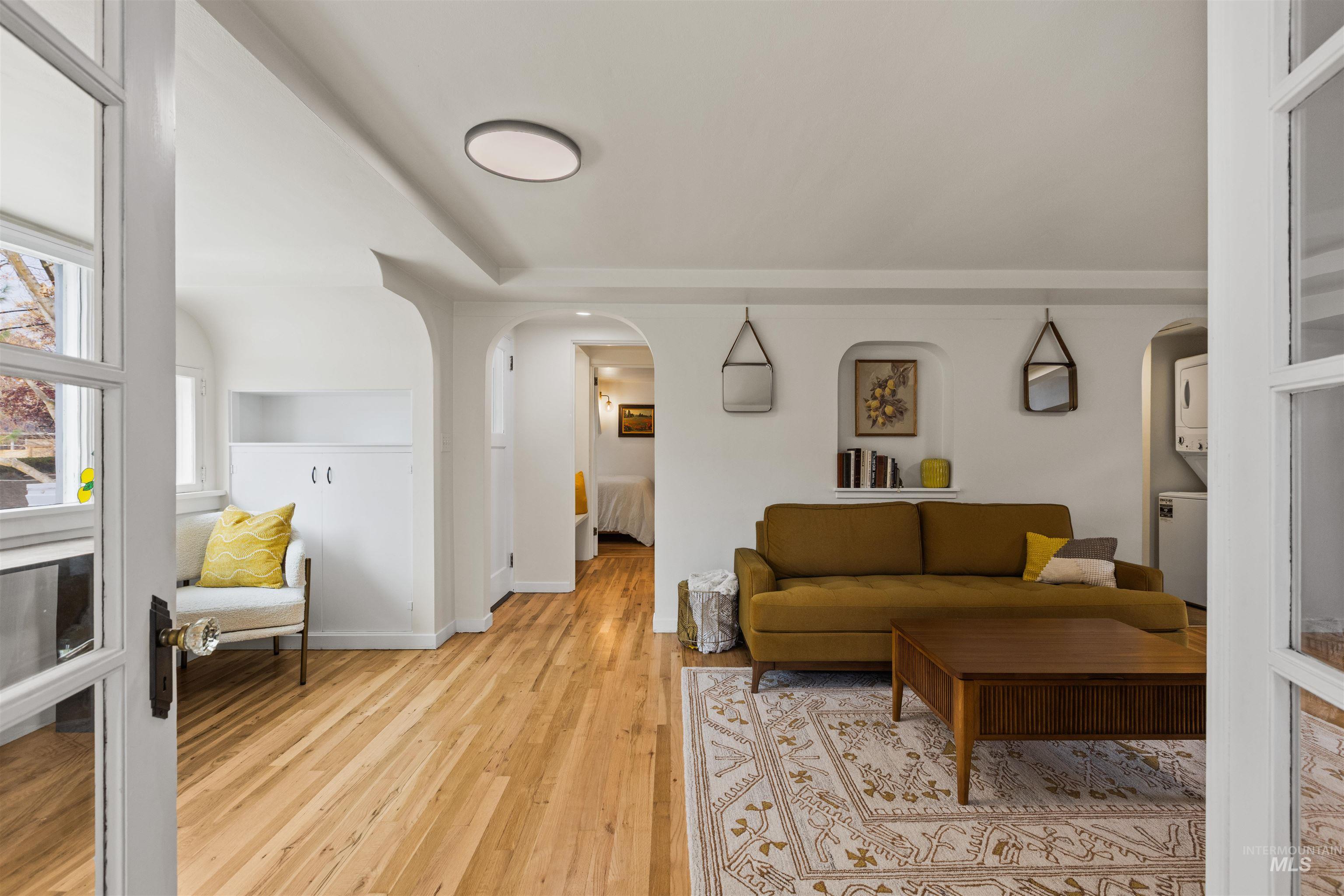 Living area with arched walkways, light wood-style floors, and estacked washer and dryer