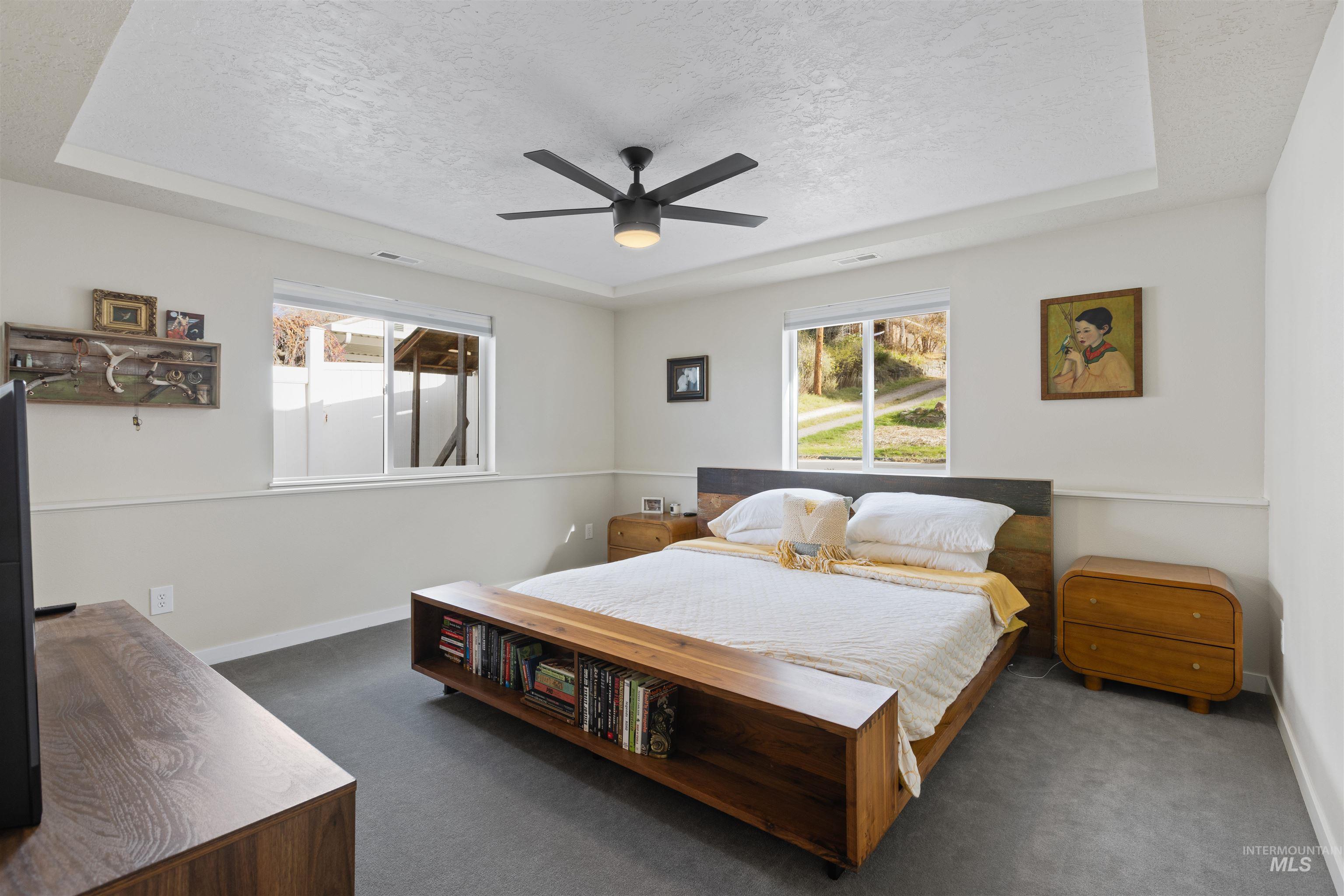 Bedroom with a tray ceiling, multiple windows, dark colored carpet, and a textured ceiling
