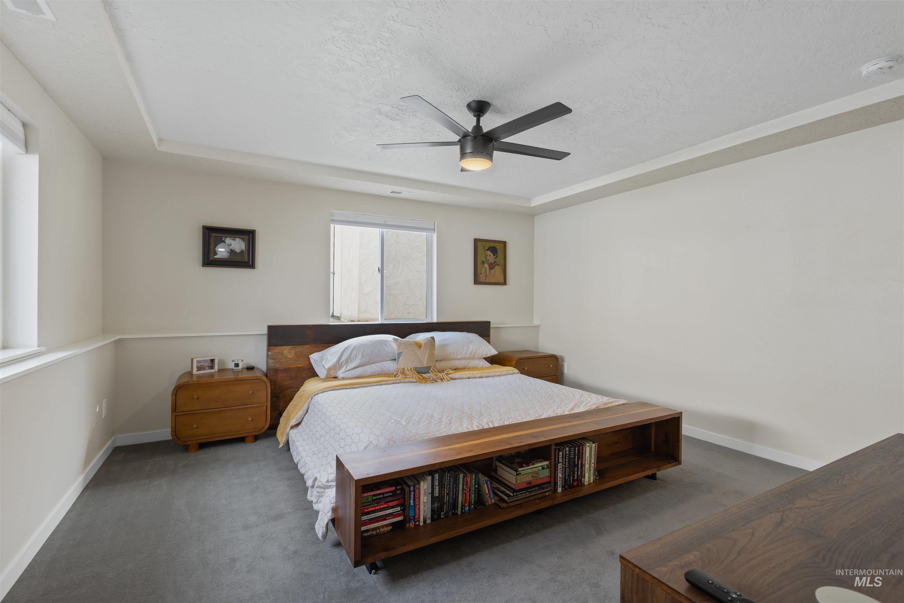 Carpeted bedroom featuring a raised ceiling, a textured ceiling, and a ceiling fan