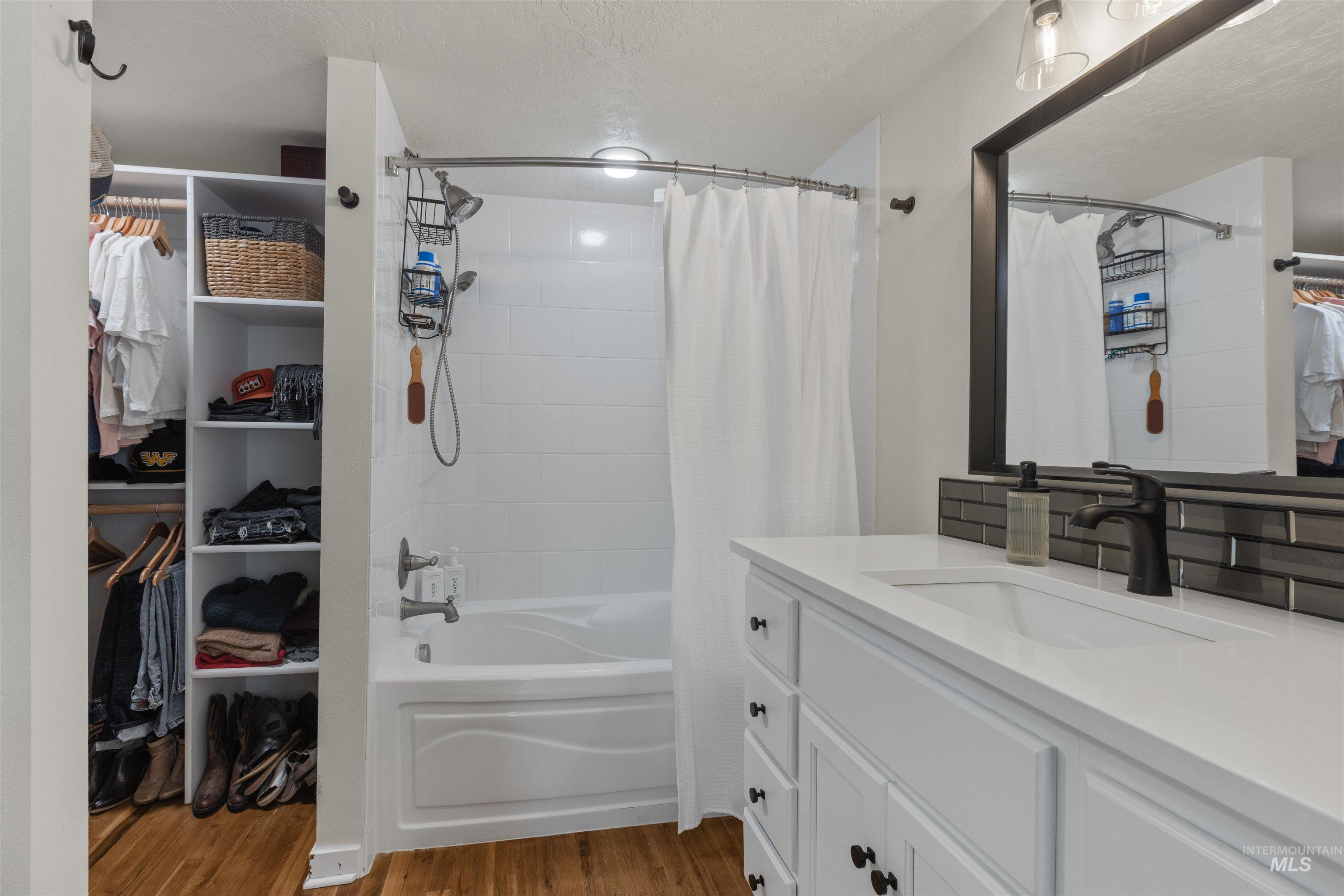 Bathroom featuring vanity, shower / bath combination with curtain, dark wood finished floors, a walk in closet, and a textured ceiling