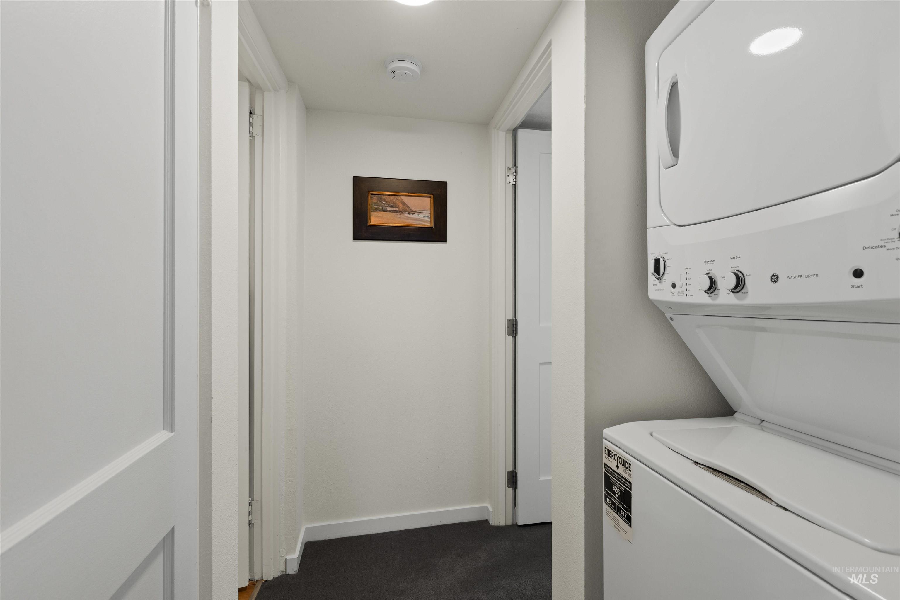 Laundry room with dark colored carpet and stacked washer / drying machine
