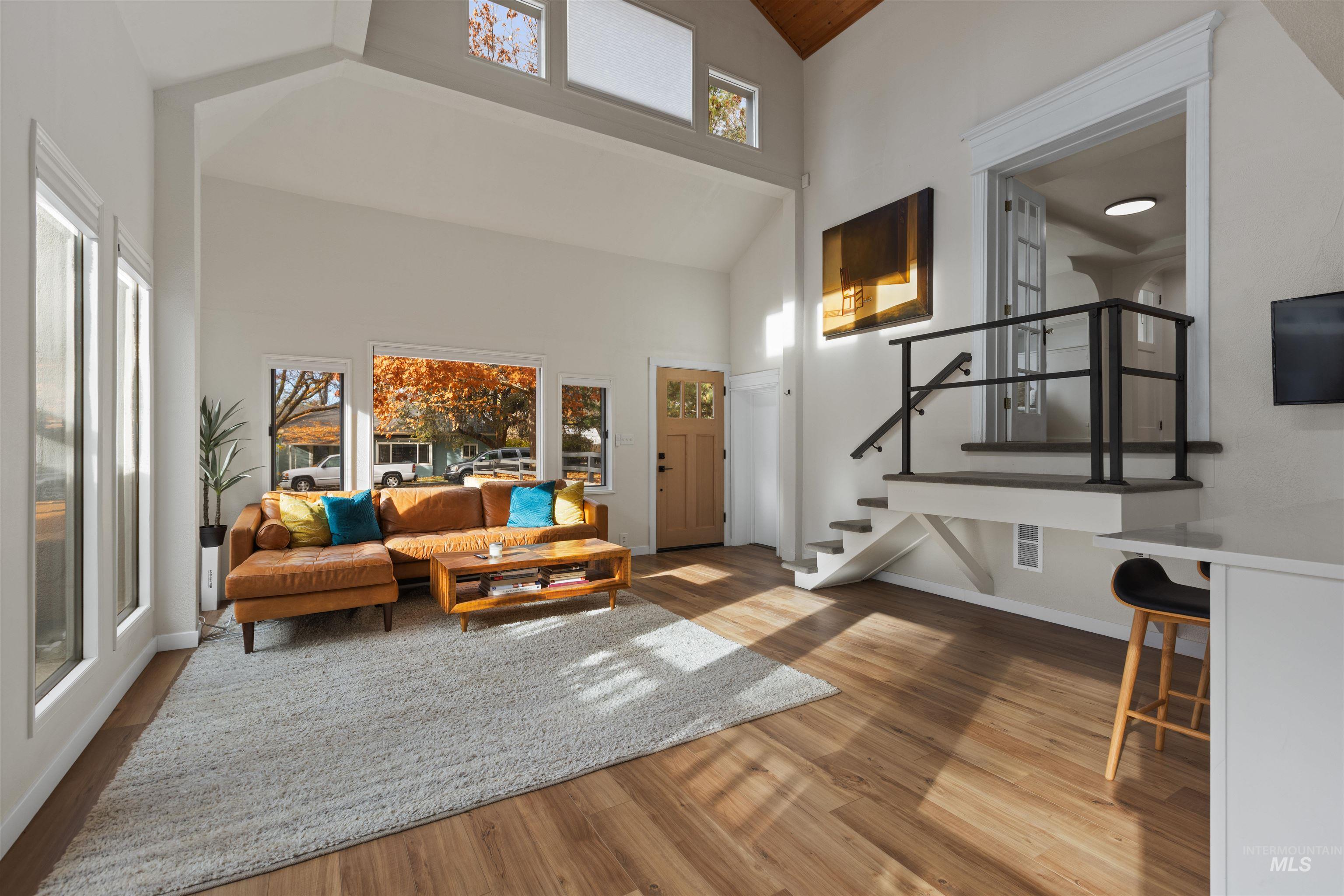 Living area featuring high vaulted ceiling, light wood-style flooring, stairway, and plenty of natural light