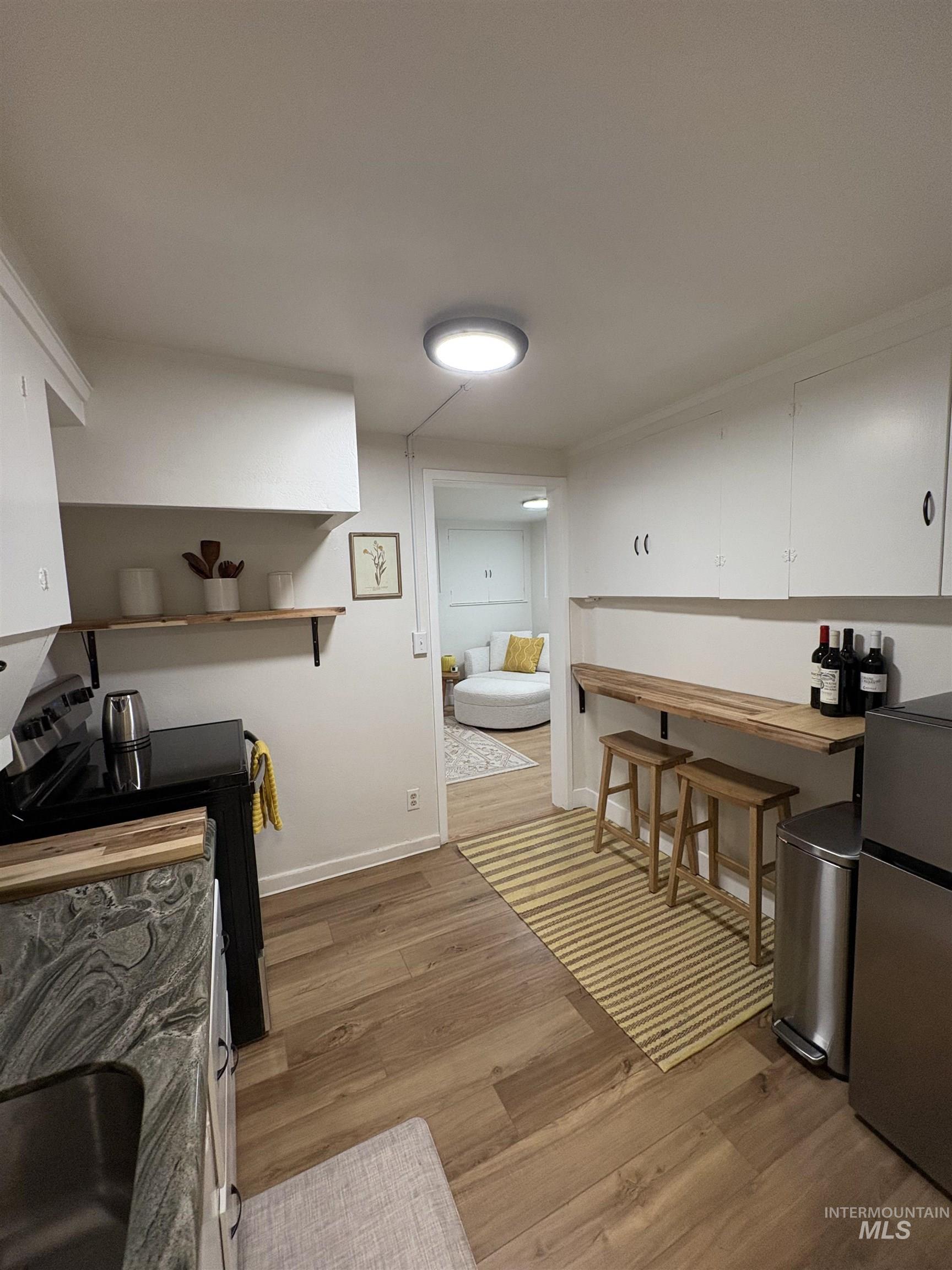 Kitchen with black electric range oven, white cabinets, freestanding refrigerator, light wood-type flooring, and open shelves