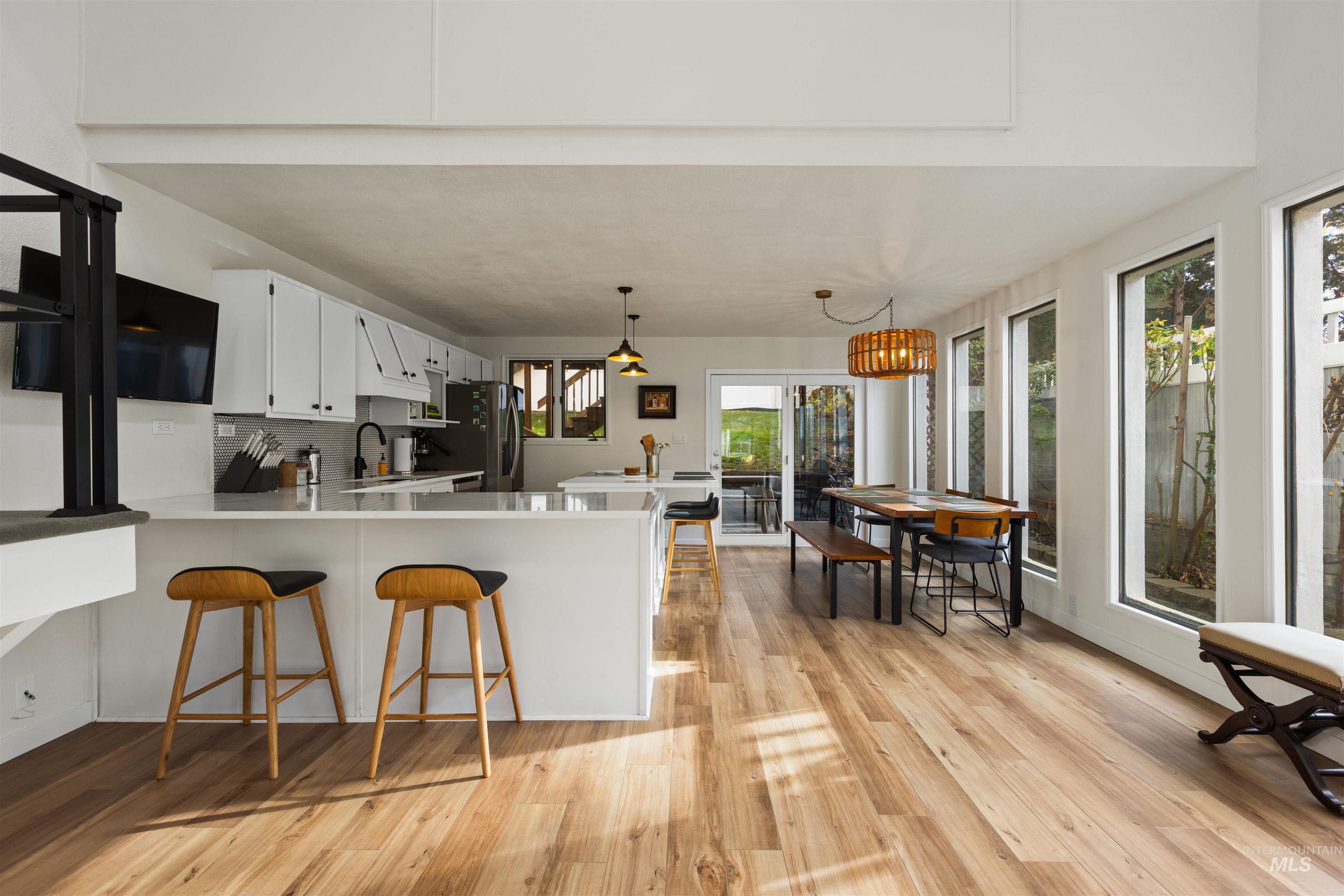 Kitchen with a breakfast bar area, decorative backsplash, white cabinets, a peninsula, and decorative light fixtures