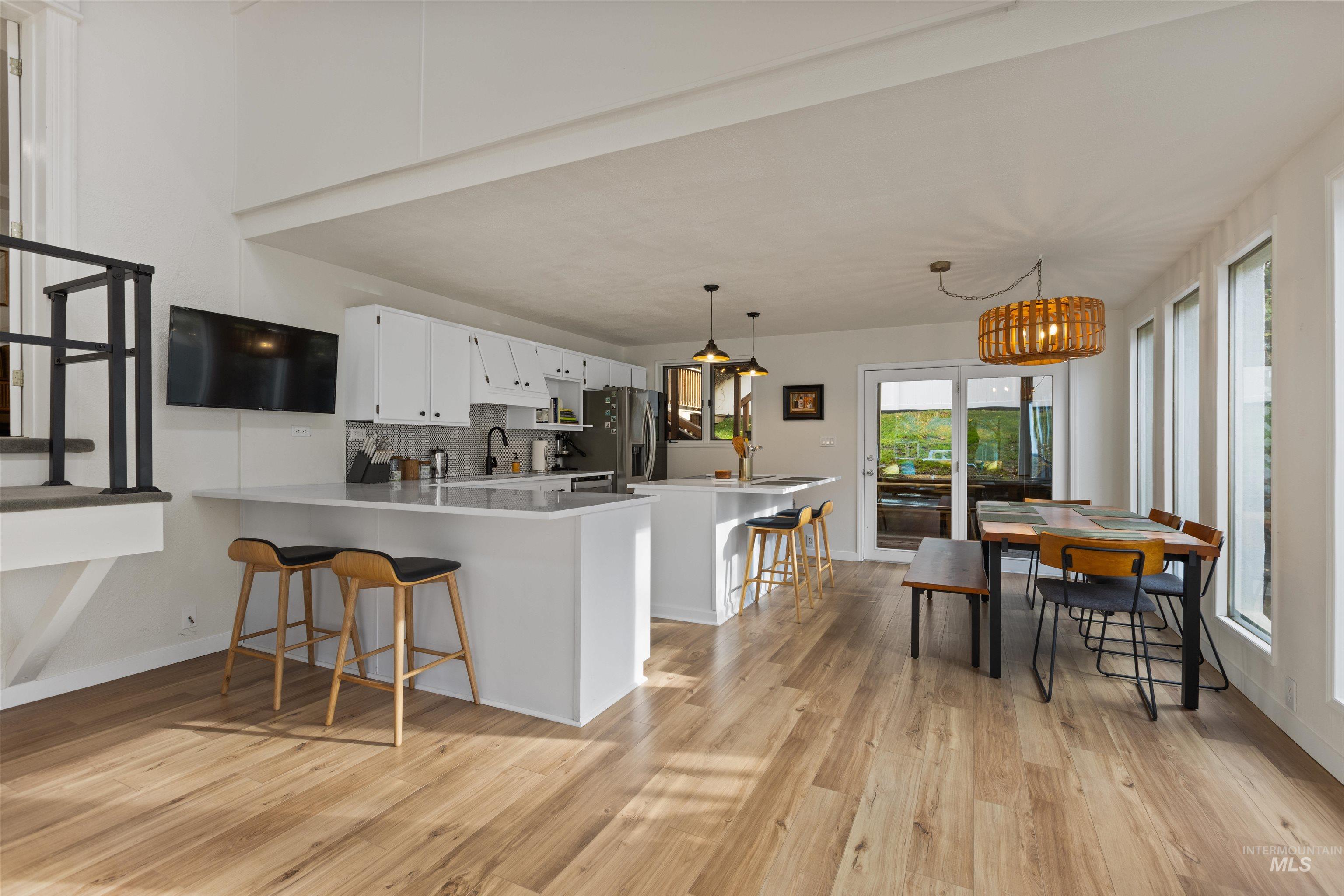 Kitchen featuring a kitchen bar, decorative backsplash, light wood finished floors, white cabinetry, and a peninsula