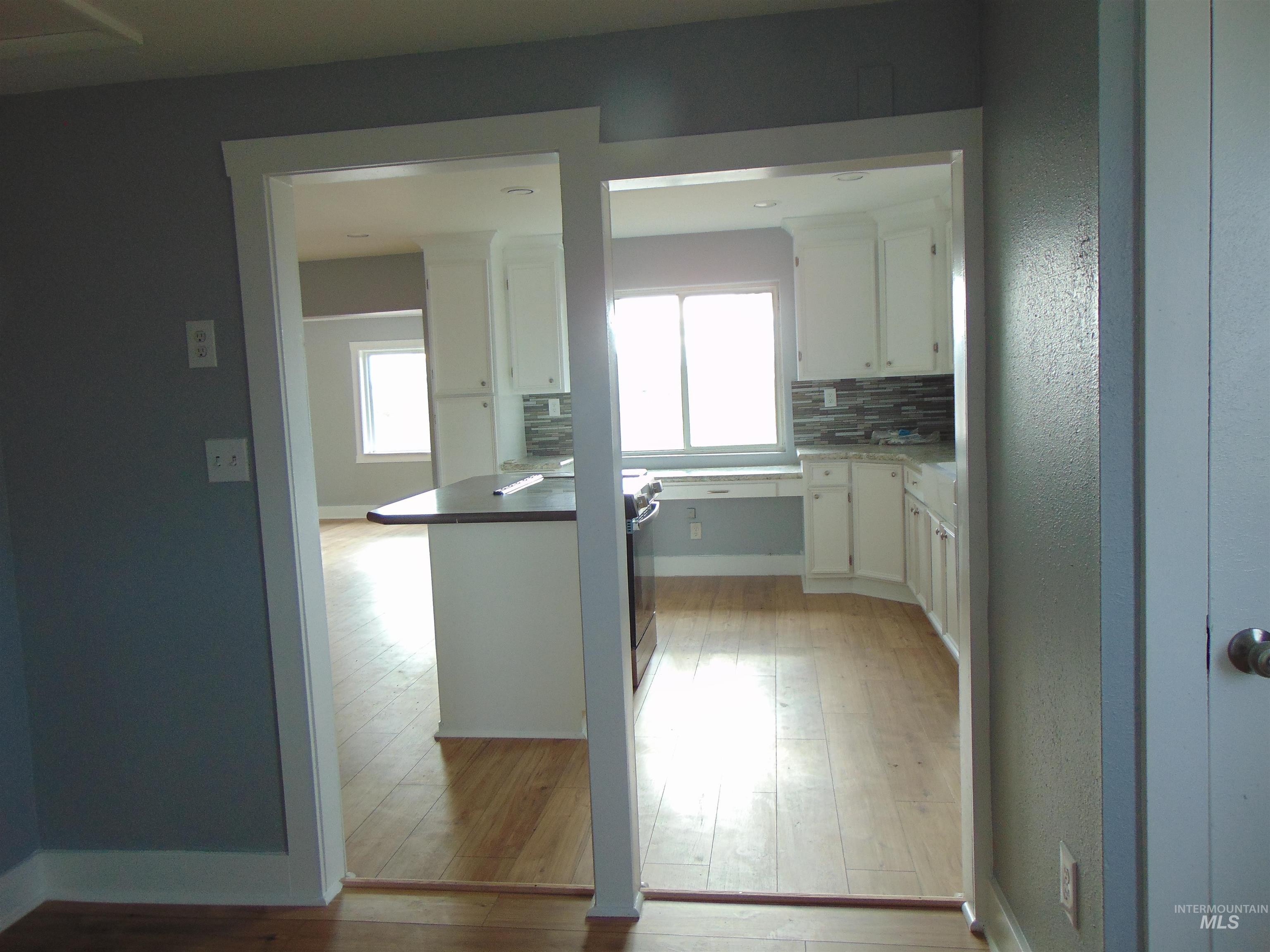 Kitchen with white cabinetry, backsplash, light wood-type flooring, and dark countertops