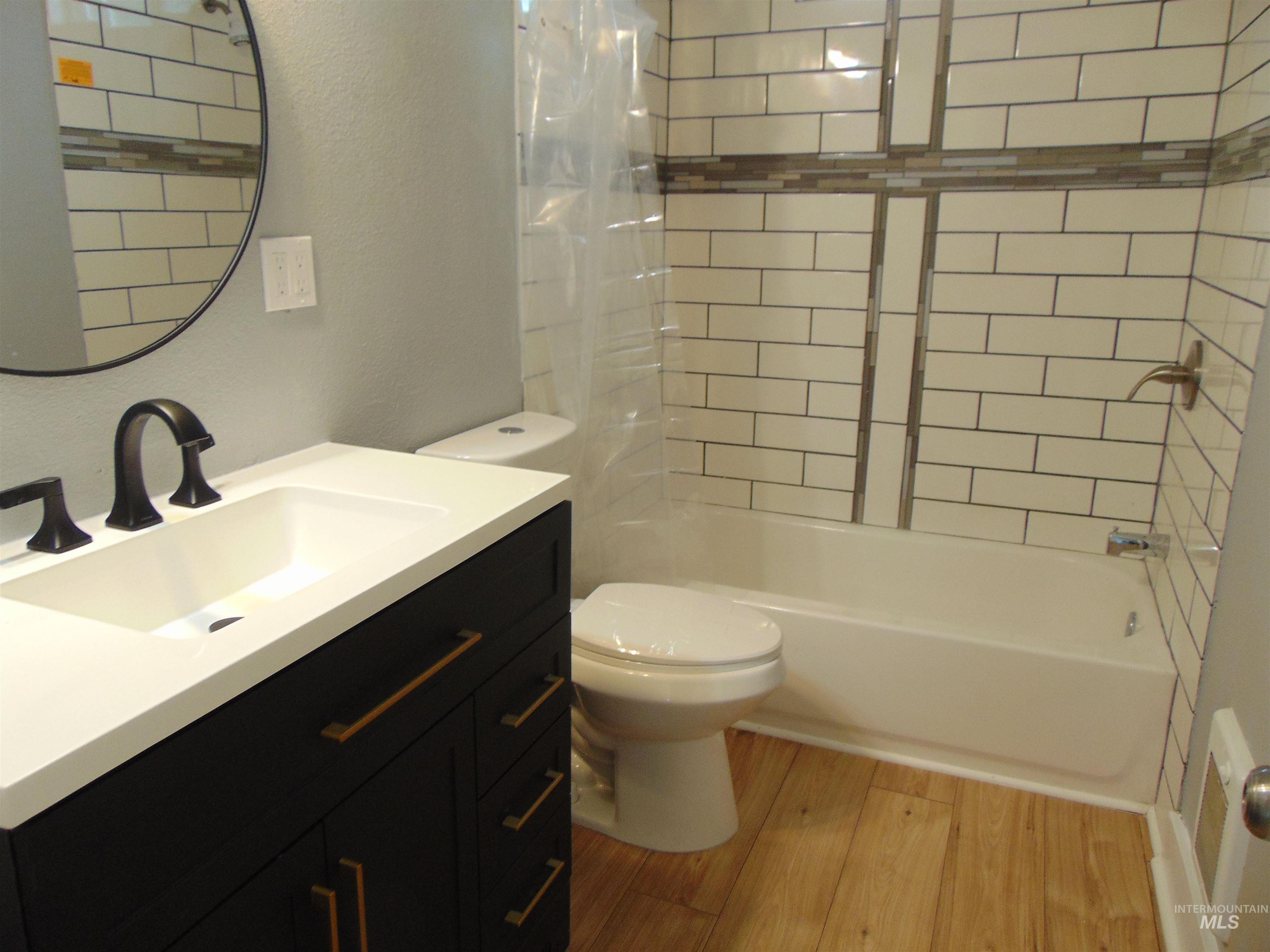 Bathroom with light wood-style floors, shower / bath combo with shower curtain, vanity, and a textured wall