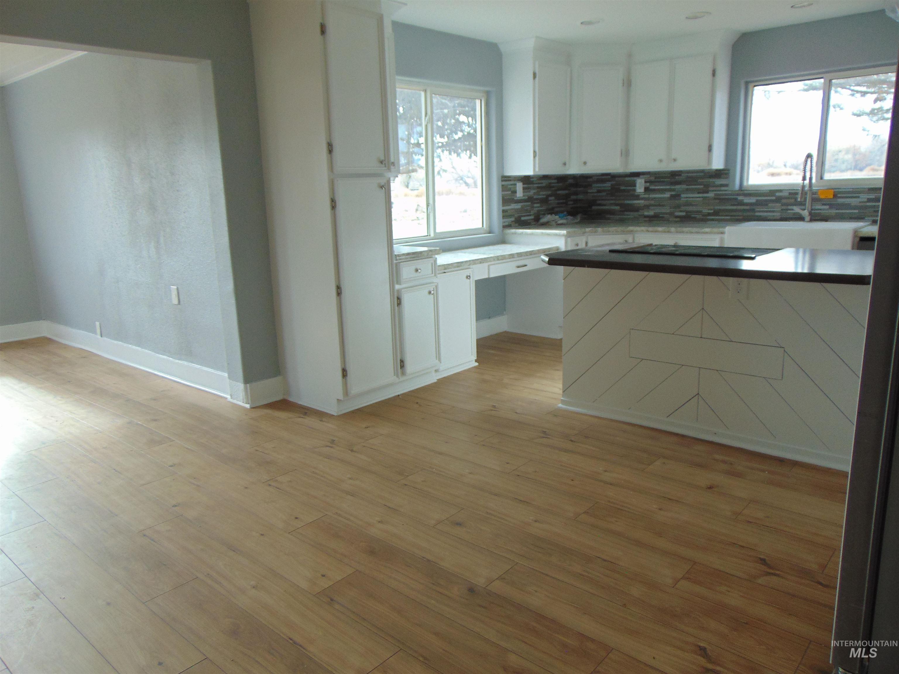 Kitchen featuring white cabinets, plenty of natural light, light wood-type flooring, and decorative backsplash