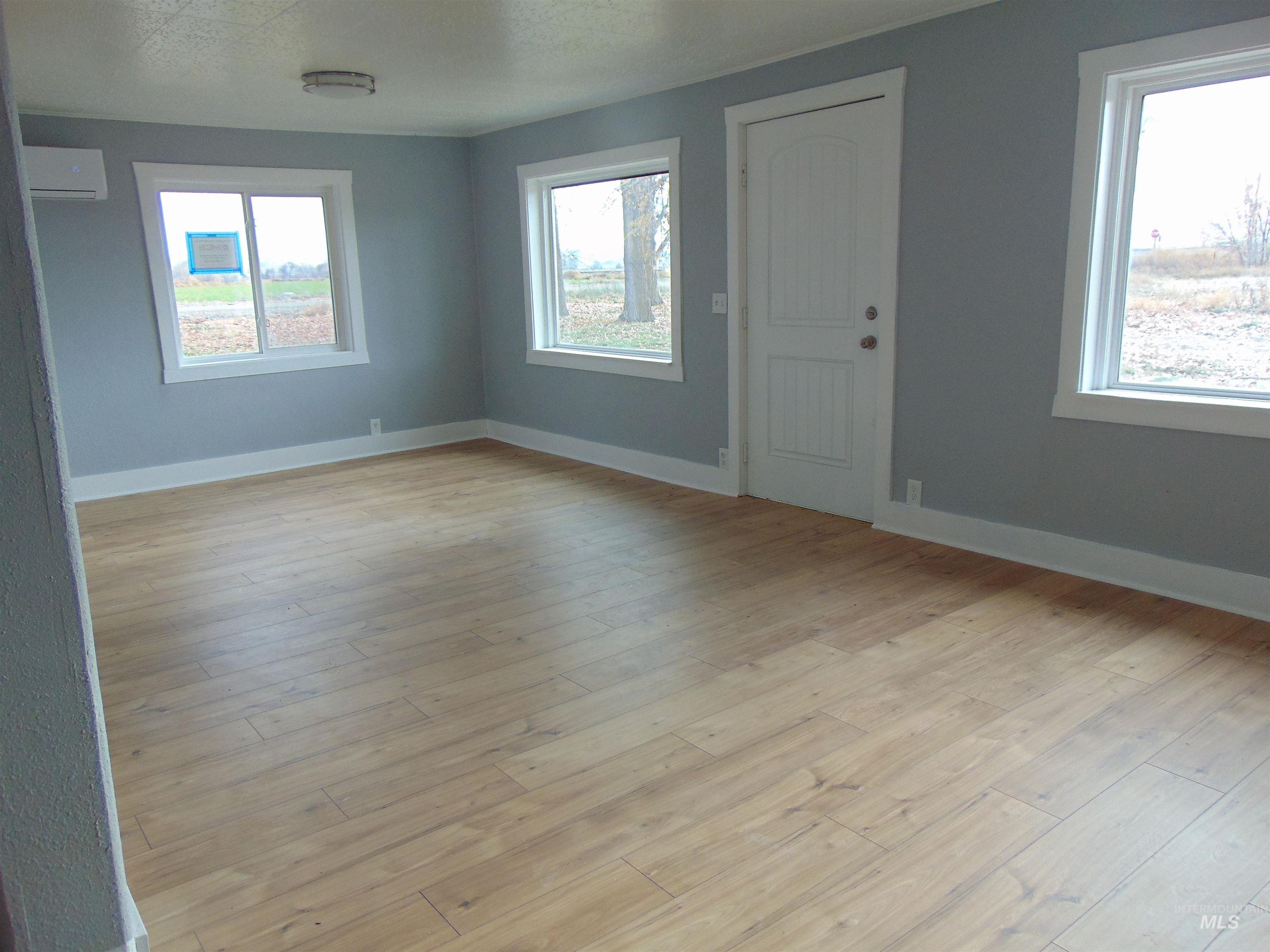 Unfurnished room featuring healthy amount of natural light, a wall mounted air conditioner, and light wood-style flooring