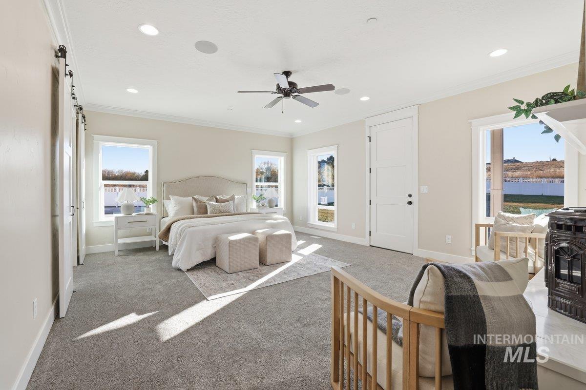 Bedroom featuring crown molding, carpet floors, a barn door, a wood stove, and a ceiling fan