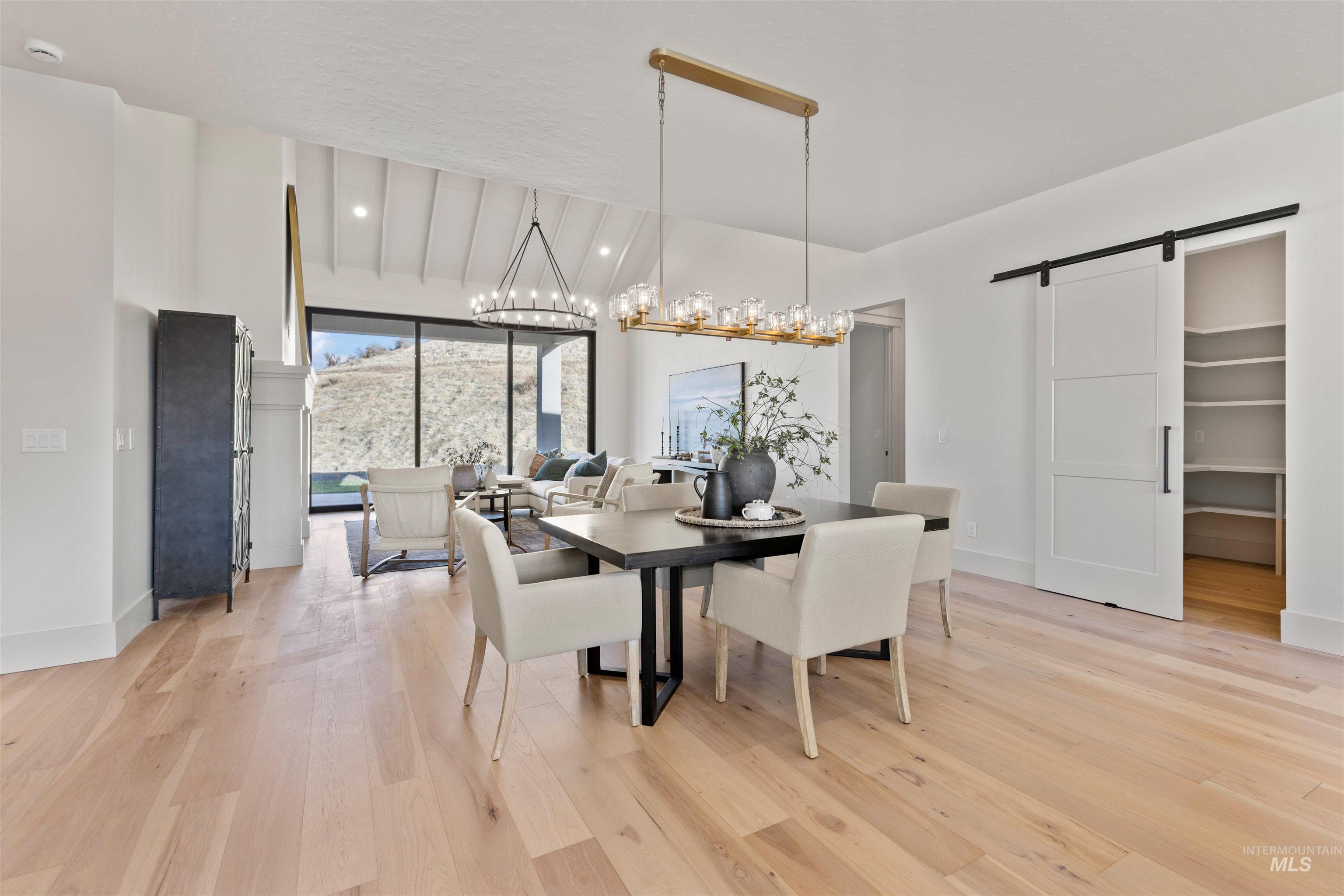 Dining area with a barn door, light wood-type flooring, recessed lighting, and vaulted ceiling