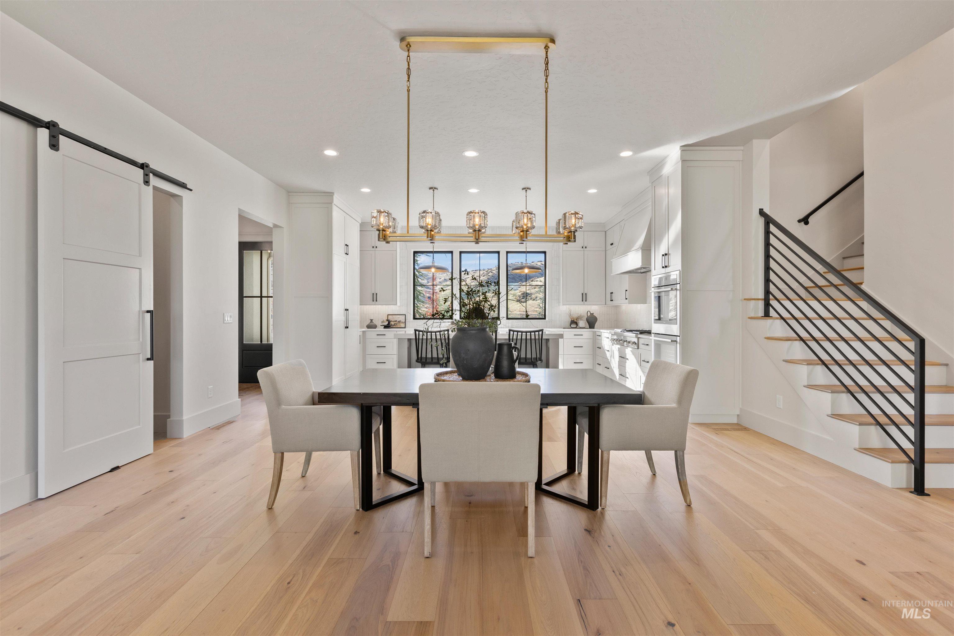 Dining space with a barn door, light wood-type flooring, recessed lighting, and stairs