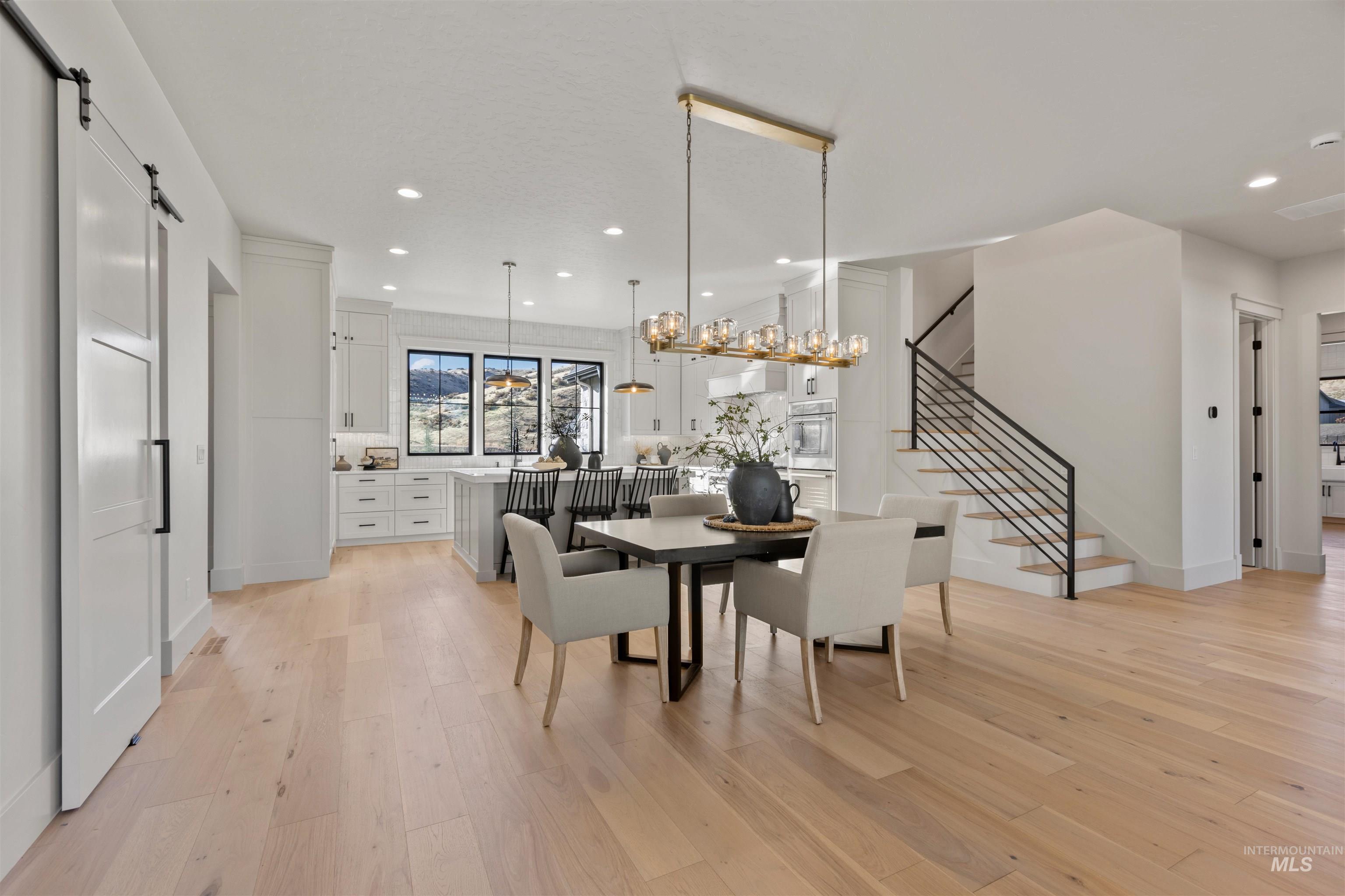 Dining room featuring a barn door, stairway, light wood-style floors, recessed lighting, and a chandelier