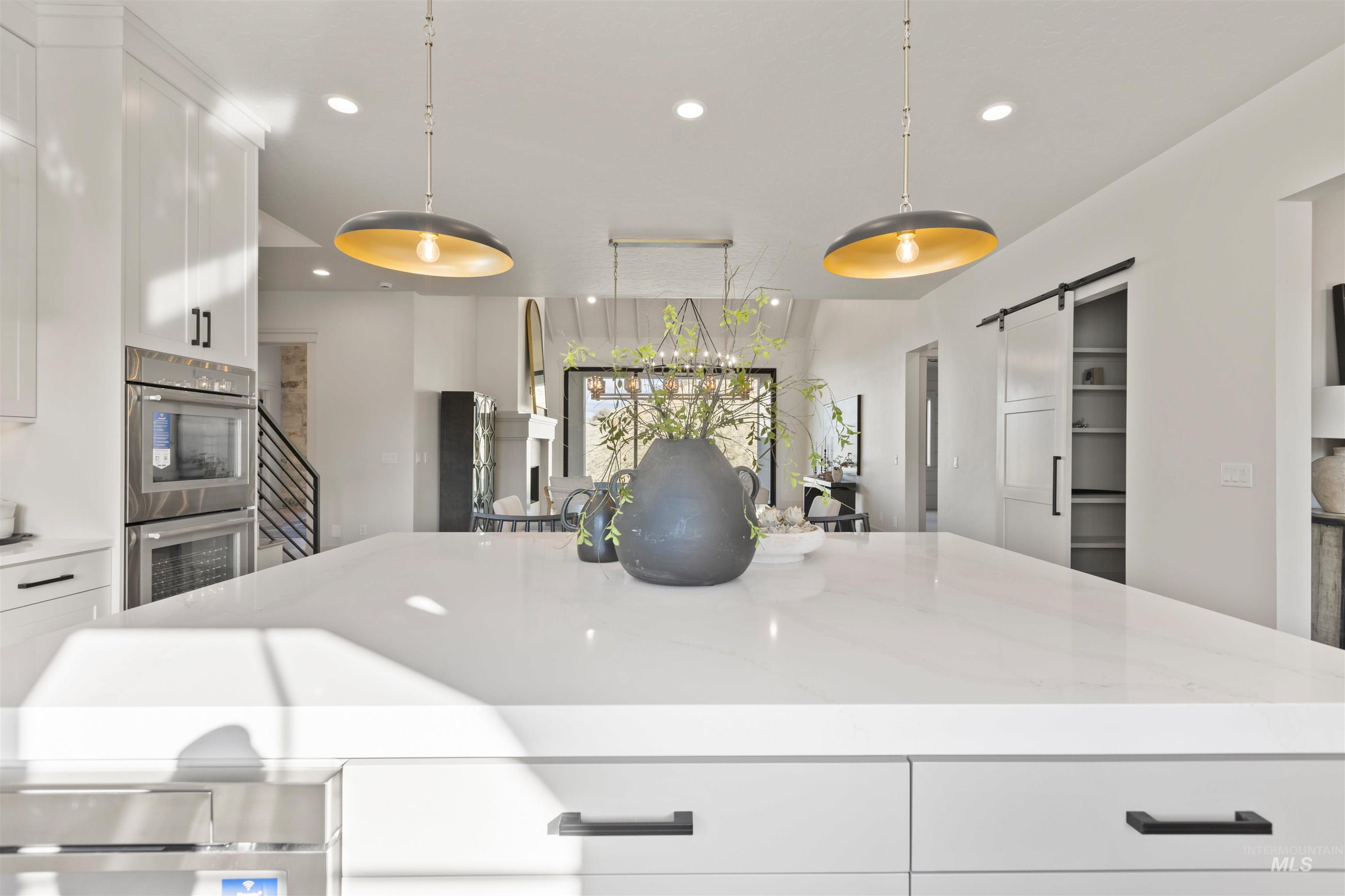 Kitchen featuring white cabinets, a barn door, recessed lighting, stainless steel double oven, and hanging light fixtures