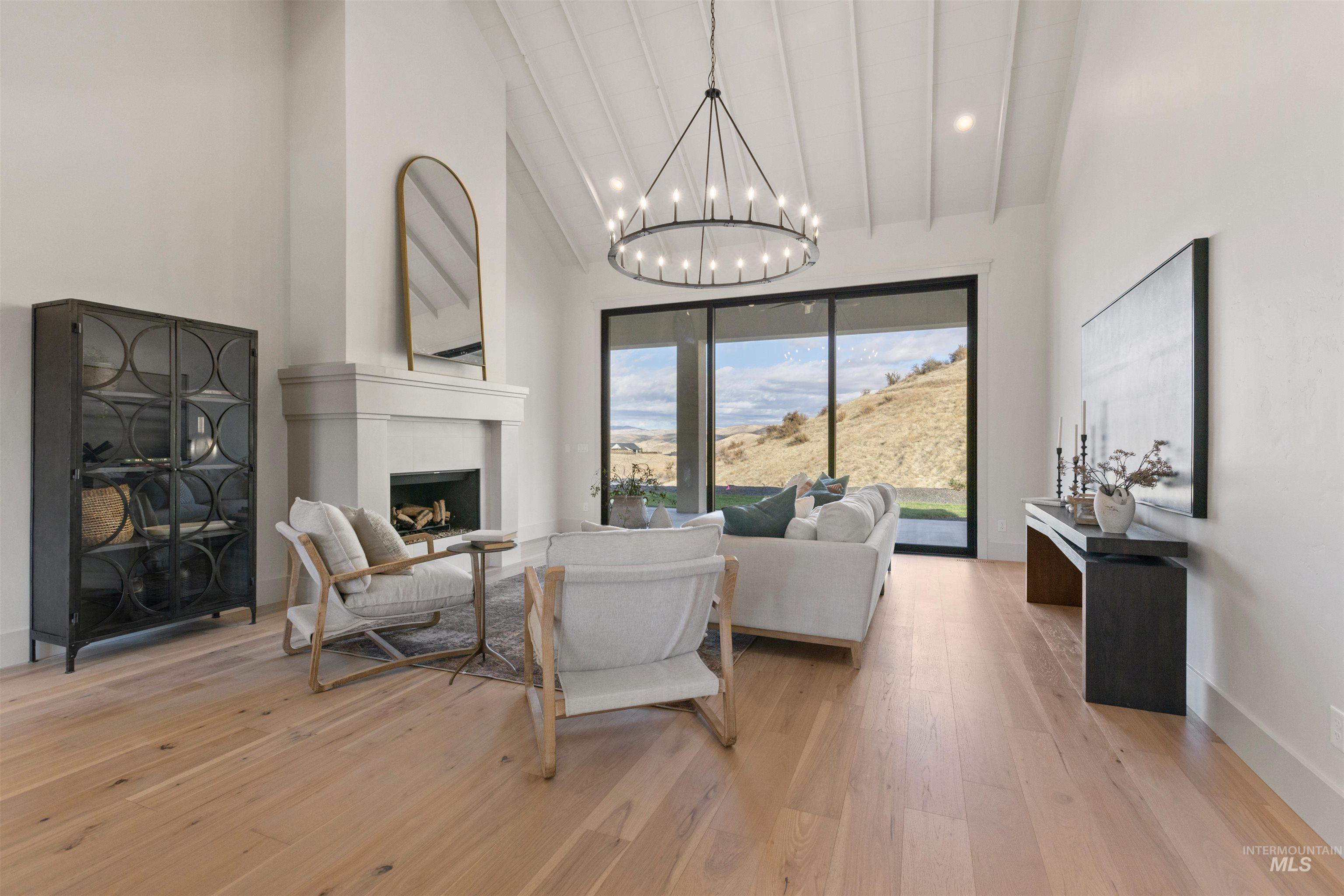 Living room with a fireplace, light wood-type flooring, high vaulted ceiling, a chandelier, and beamed ceiling