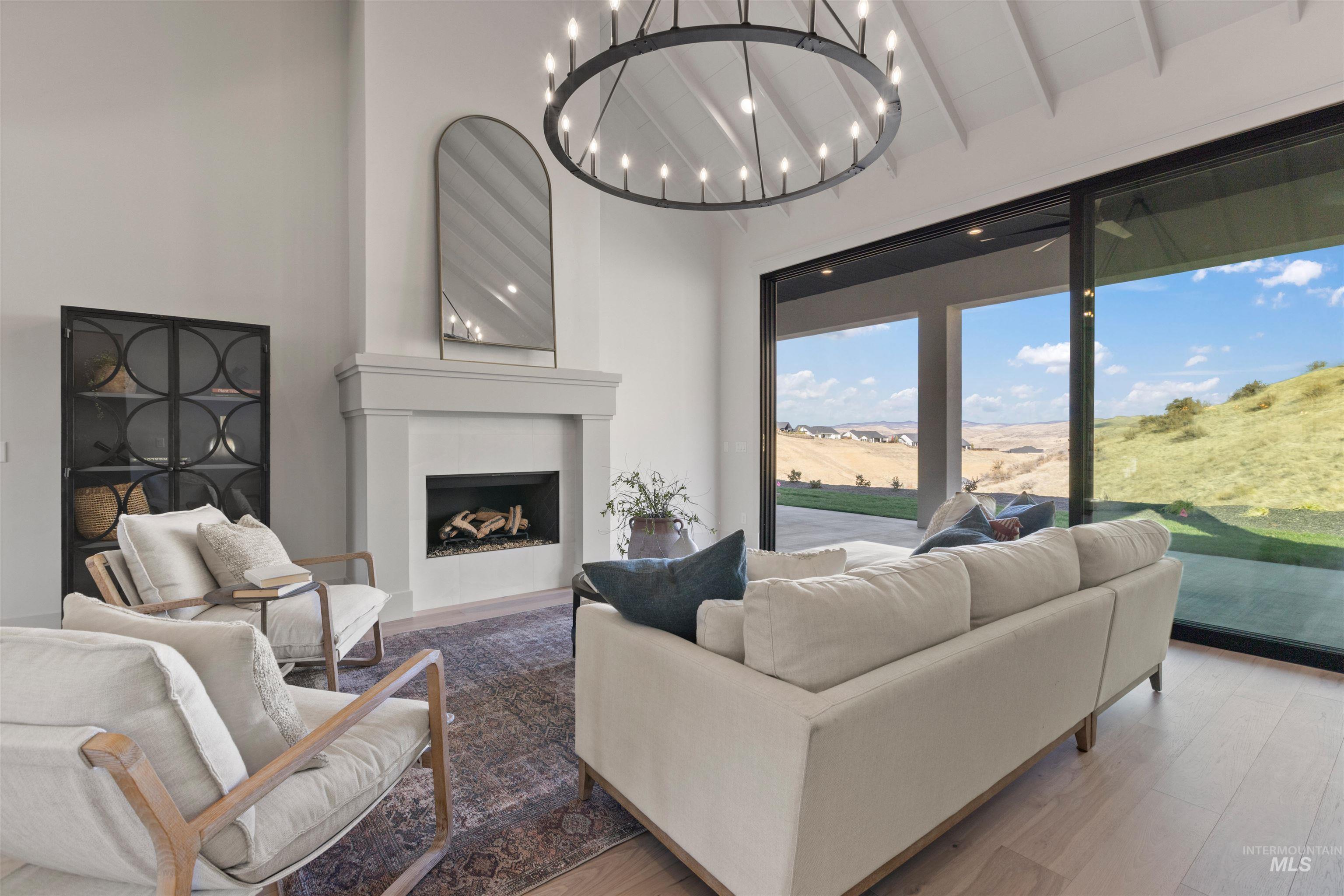 Living room with a fireplace, wood finished floors, high vaulted ceiling, a chandelier, and beam ceiling