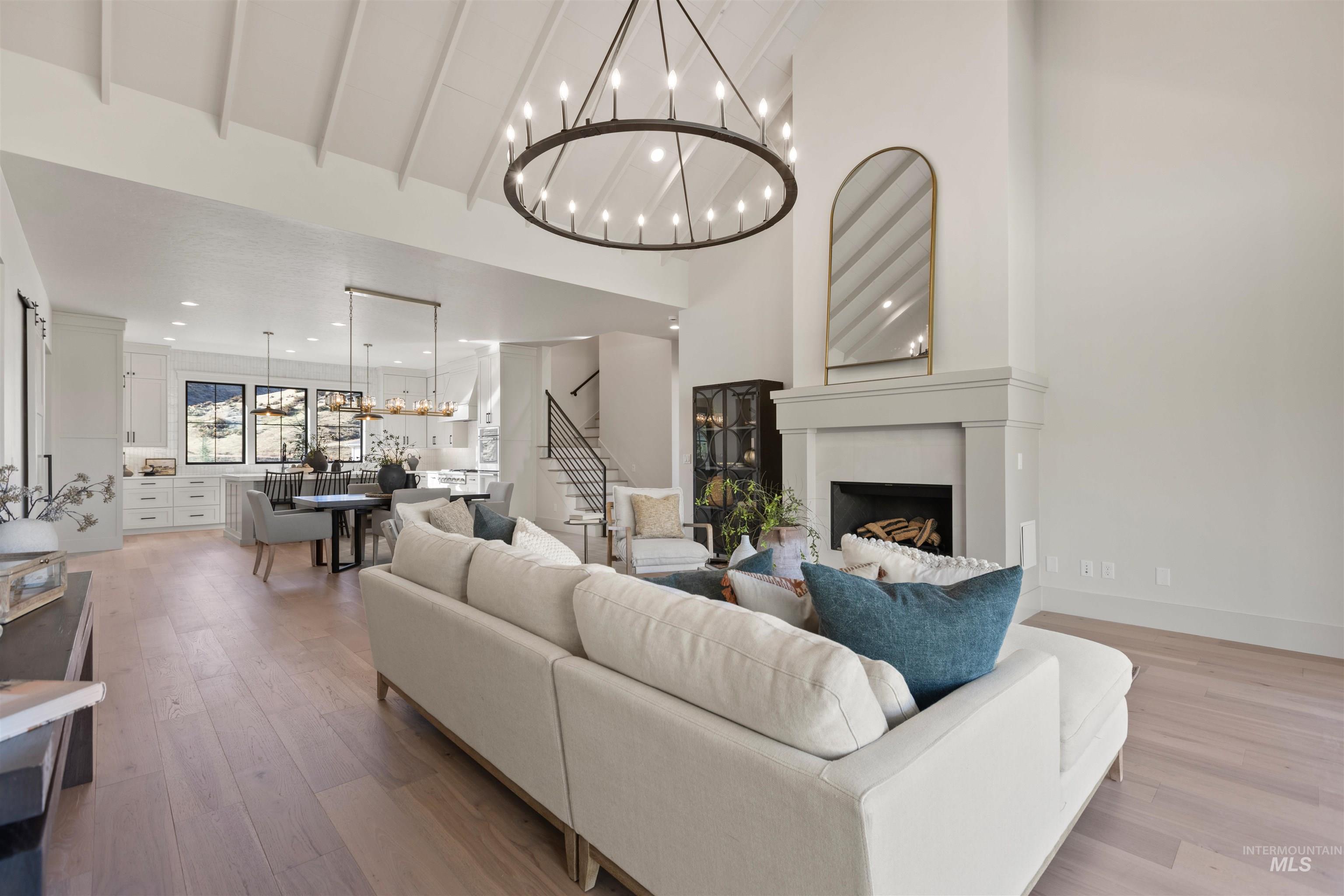 Living area featuring beamed ceiling, a fireplace, light wood-type flooring, a chandelier, and stairs